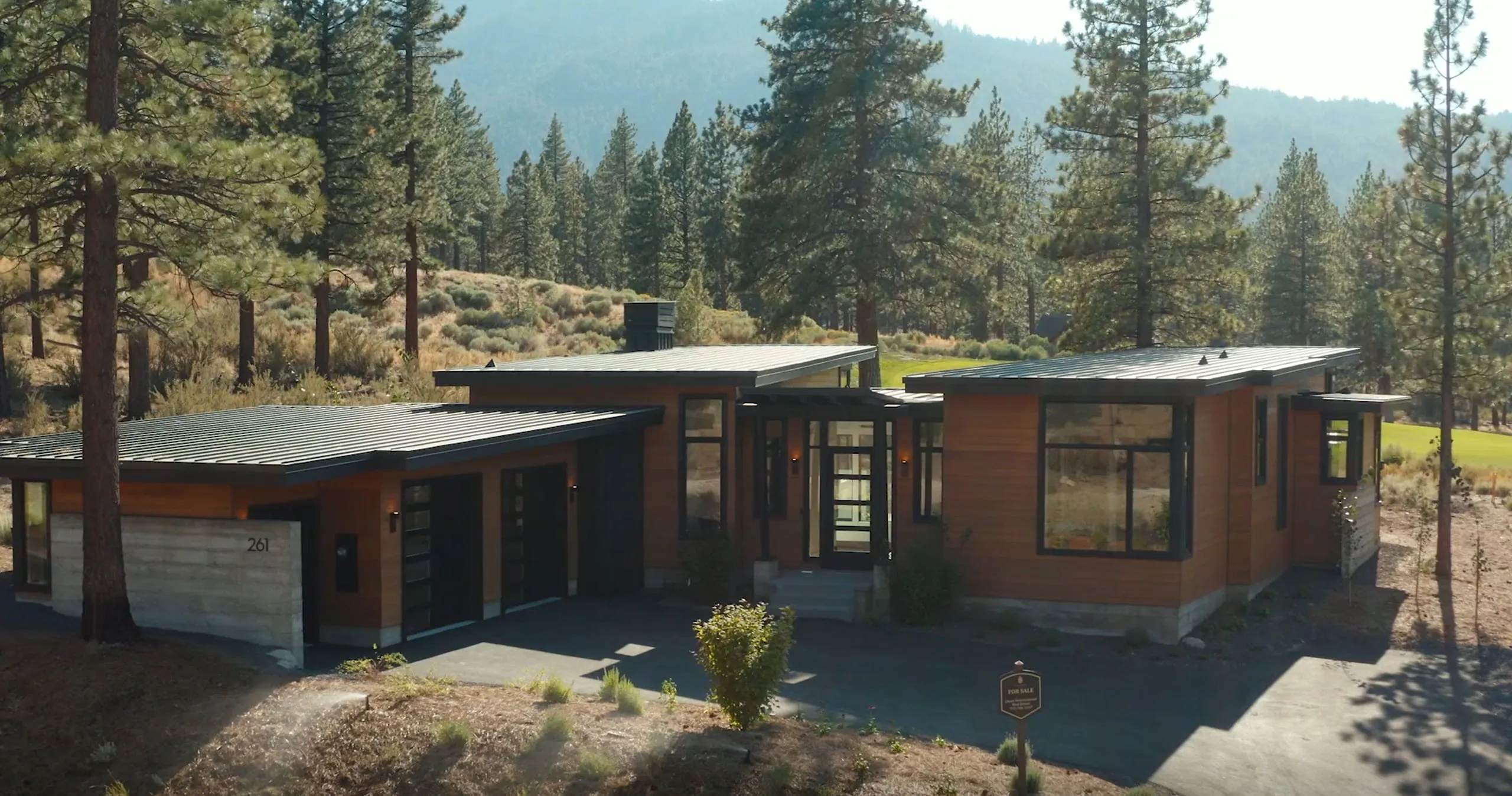 Mountain home with low metal shed roofs, wood and board-formed concrete walls and large dark-framed windows among pines