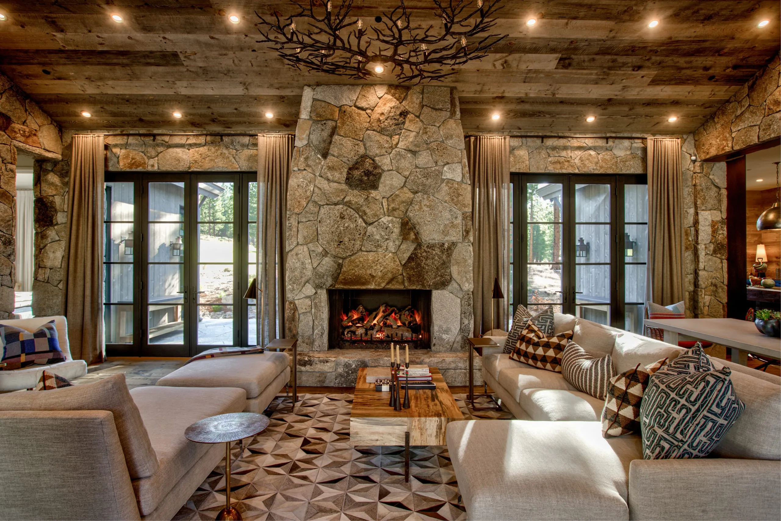 Interior living room with a tall rough stone fireplace, reclaimed wood ceiling, French doors and sectional sofas