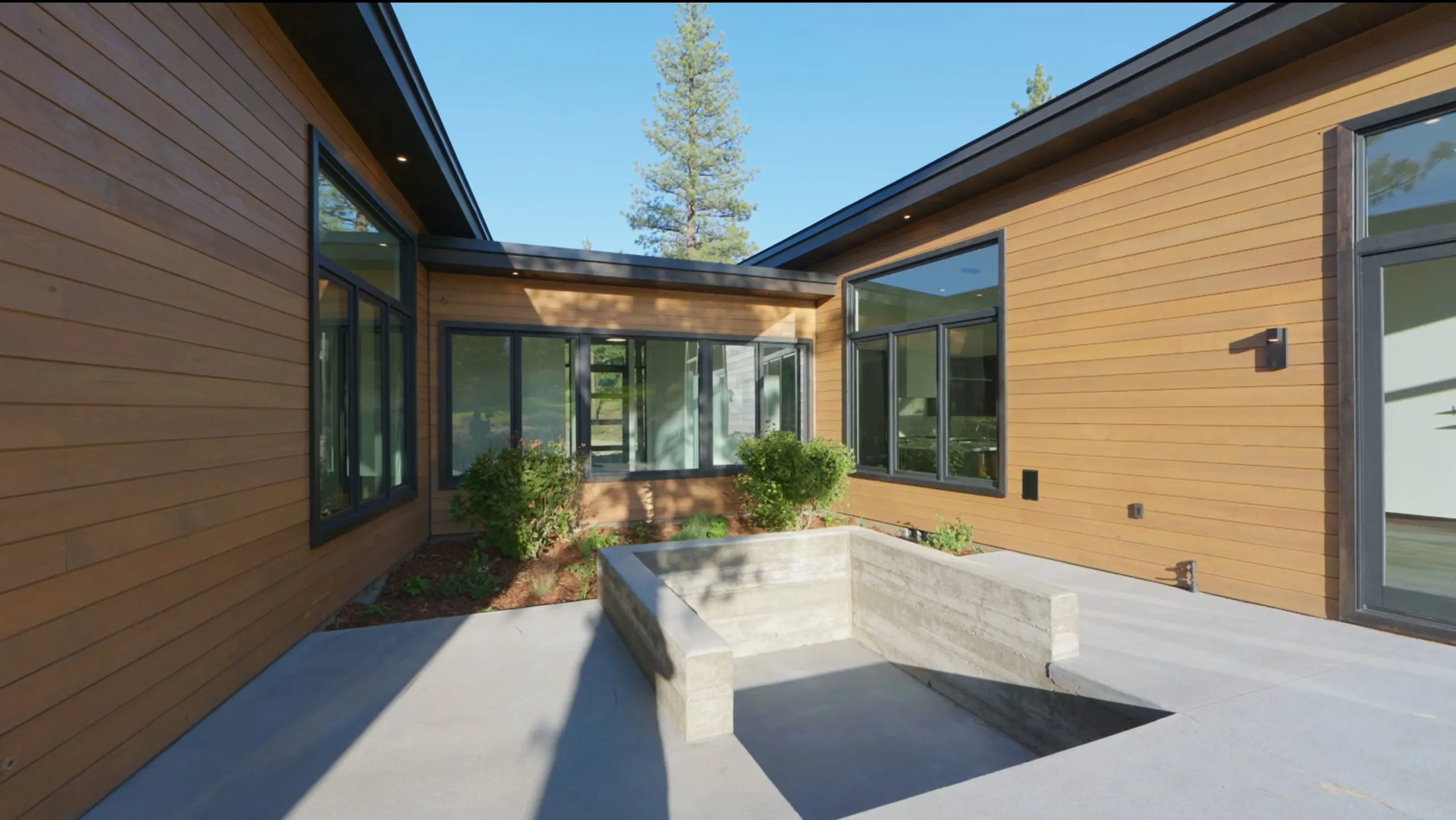 Courtyard between wood-clad wings with large windows, a concrete patio and a sunken board-formed concrete seating pit