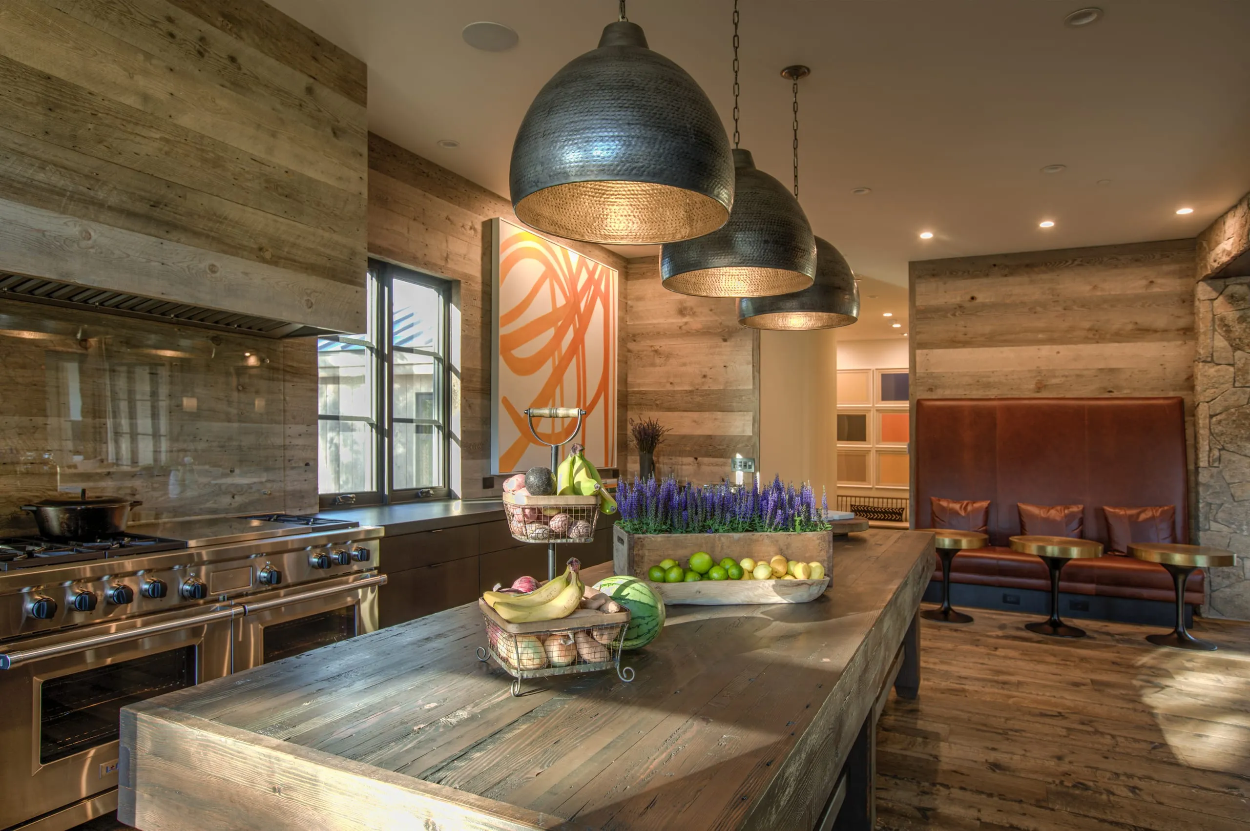 Kitchen with reclaimed wood walls, island with fruit and lavender, copper-lined pendants and a leather banquette beyond