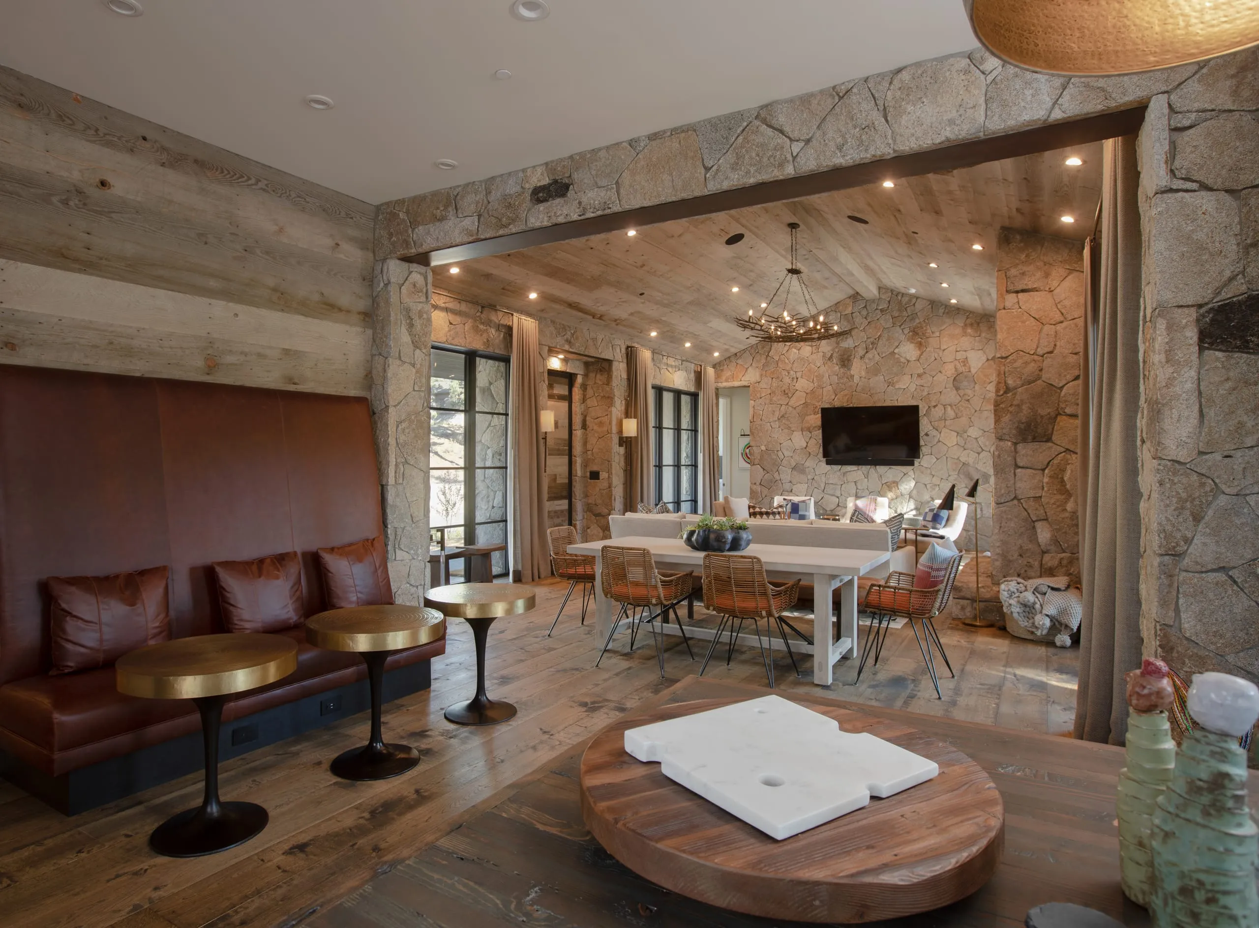 Interior looking from a leather banquette and brass tables through a stone archway to a dining area and vaulted living room