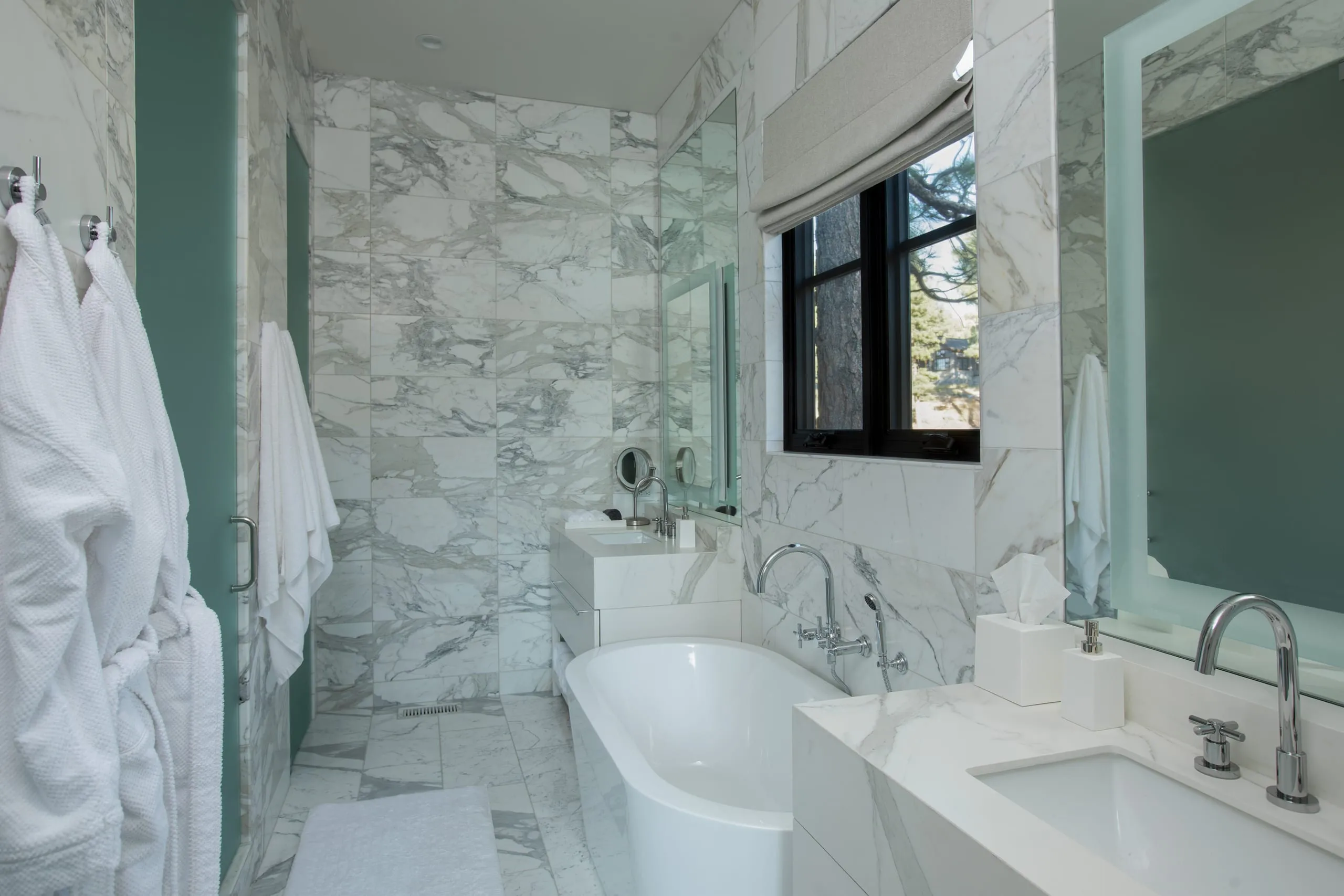 Bathroom with white marble walls and floor, freestanding tub, double vanity, black-framed window and glass shower