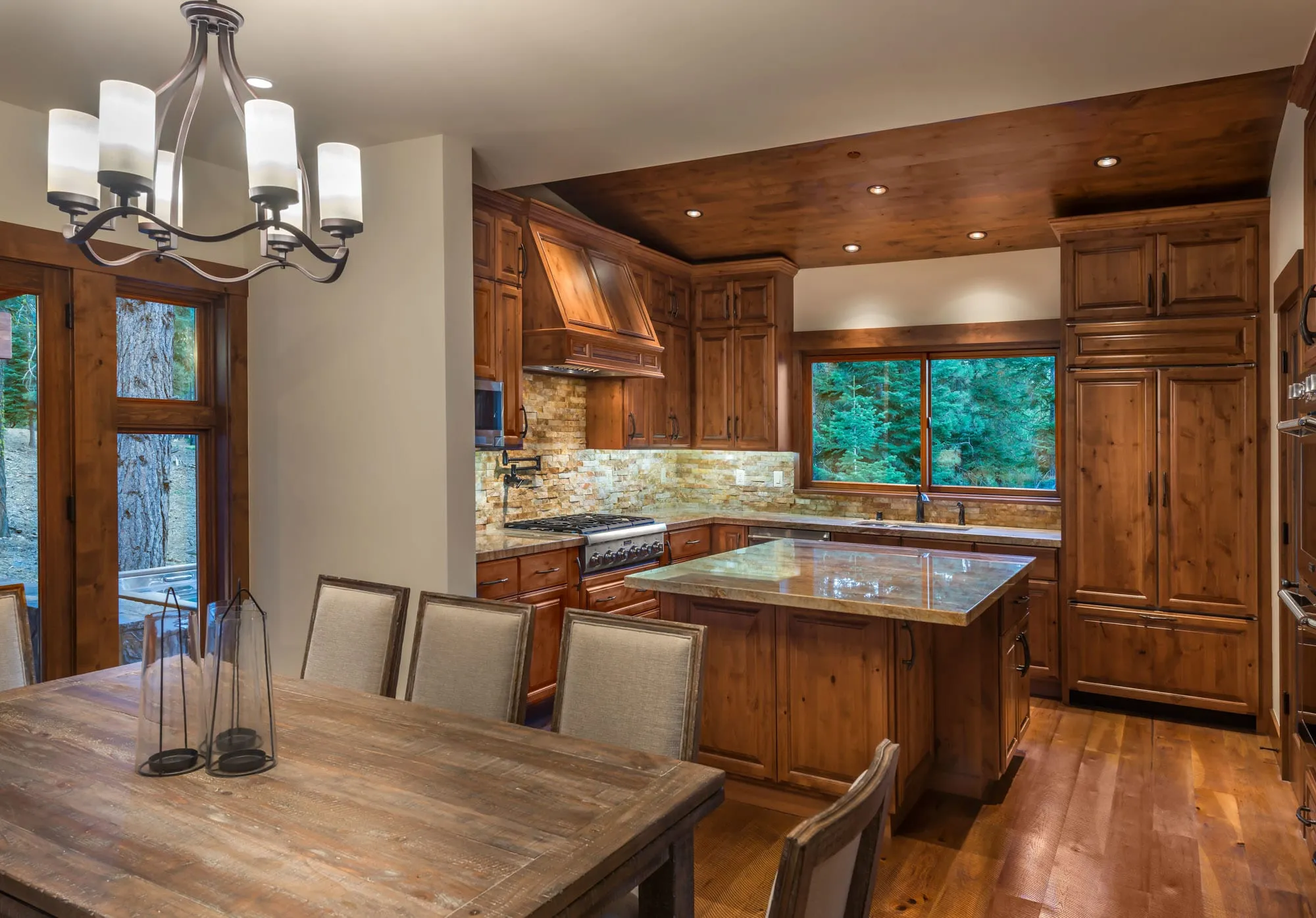 Kitchen with knotty alder cabinets, stone backsplash, a copper-toned hood, island with stone top and a window to evergreens