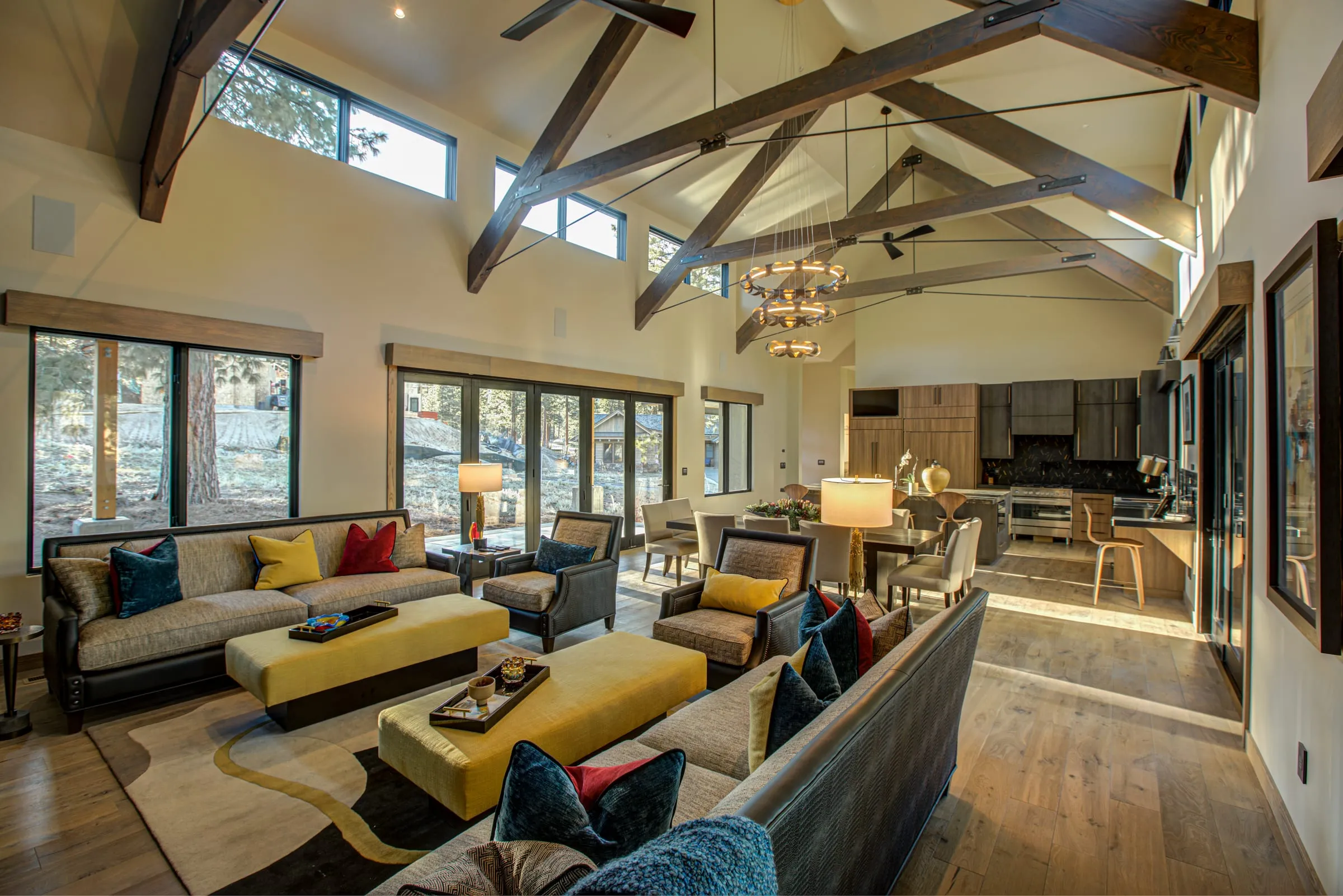 Vaulted great room with timber trusses and steel rod ties, clerestory windows, yellow ottomans and the kitchen beyond