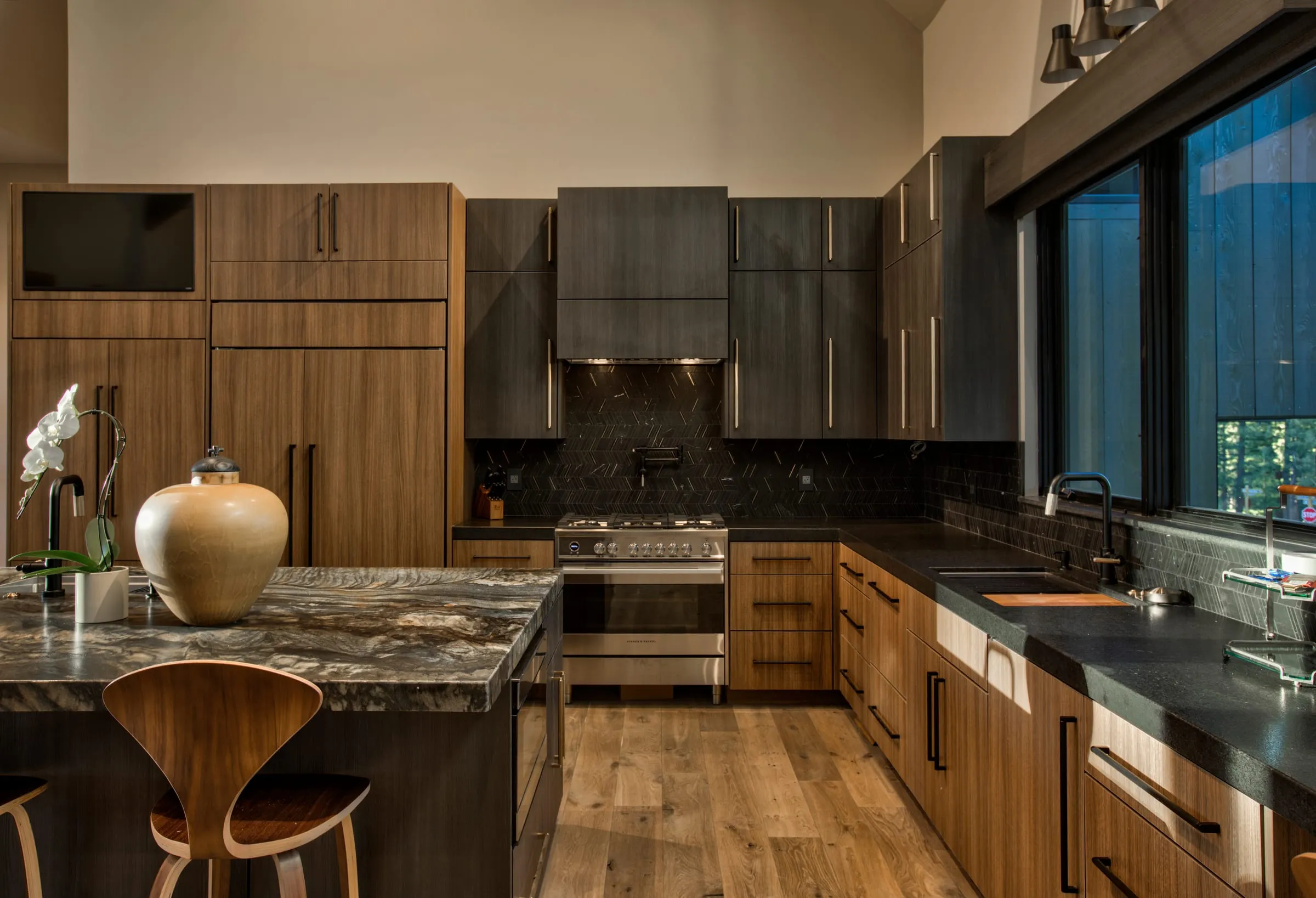 Kitchen with walnut and dark cabinets, a stone-topped island with a molded wood stool, a stainless range and black counters under the windows