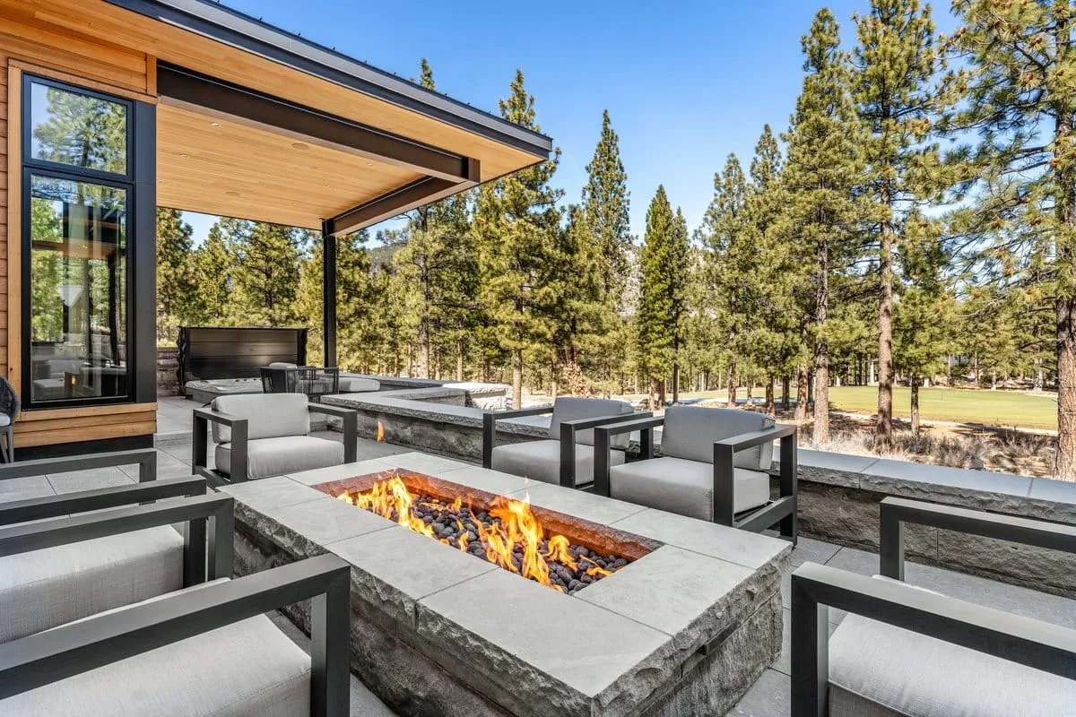 Stone fire table with lounge chairs on a terrace under a deep roof overhang, looking out to pines and a golf fairway