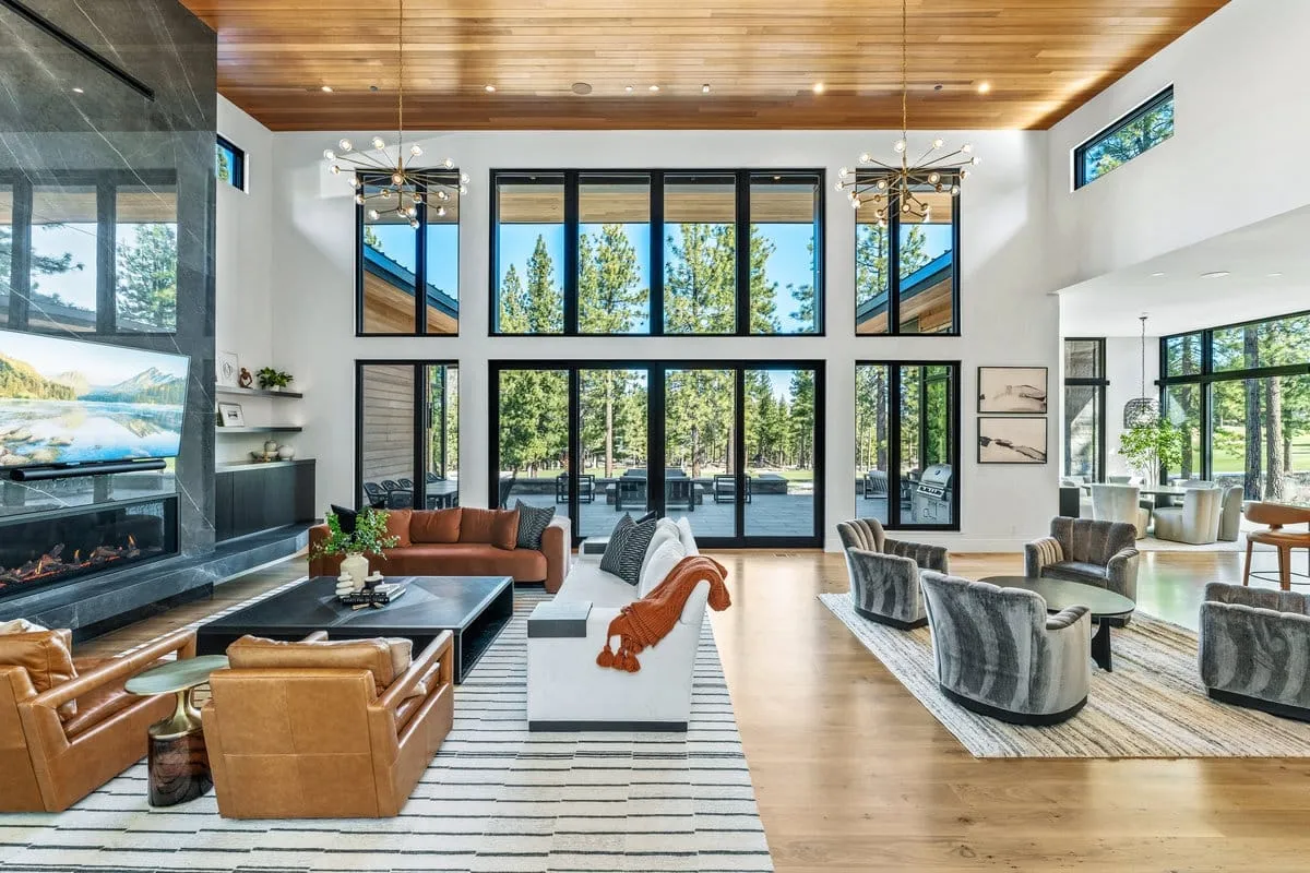 Great room with a cedar ceiling, tall black-framed windows, a stone fireplace wall, two seating areas and the dining area beyond