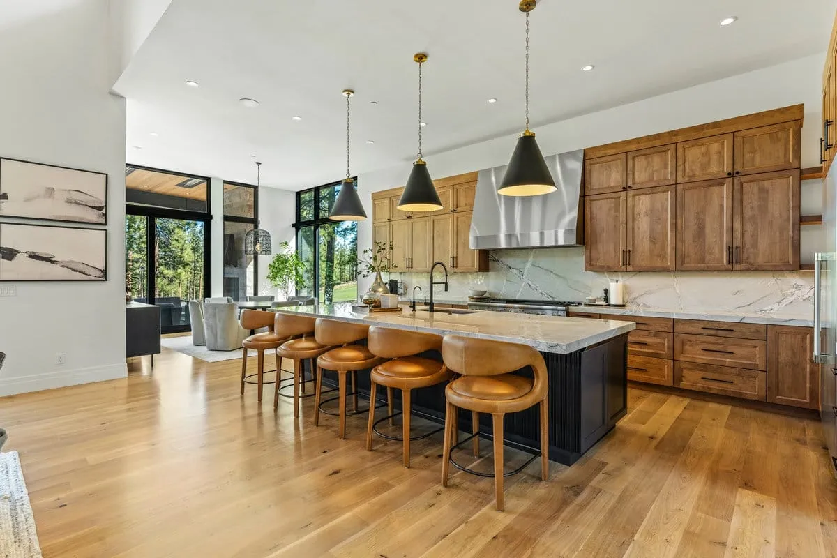 Kitchen with warm wood cabinets, a long island with leather stools, black pendant lights and a stainless hood