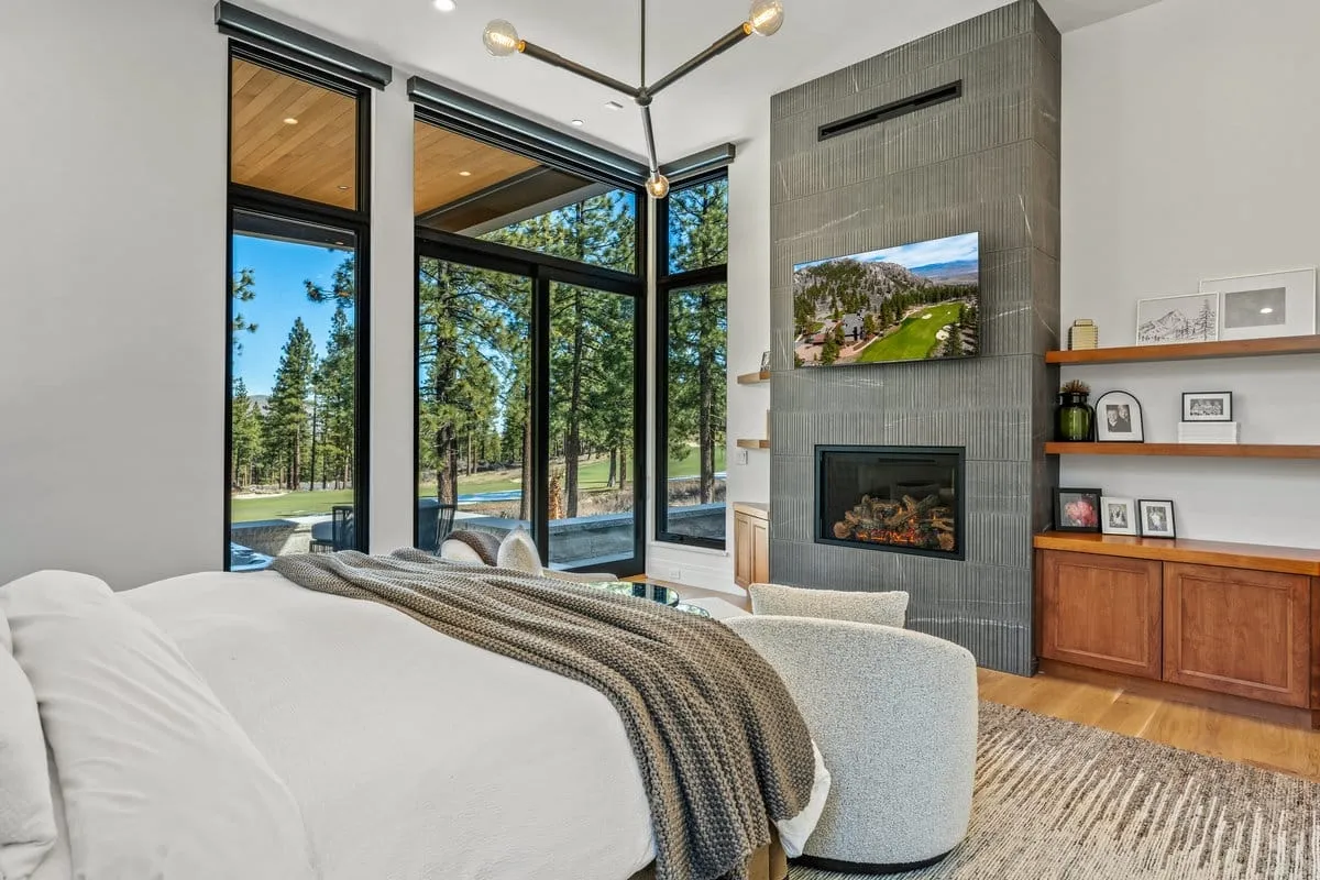 Bedroom with a tiled fireplace wall, wood shelves and corner windows looking out to pines and the golf course