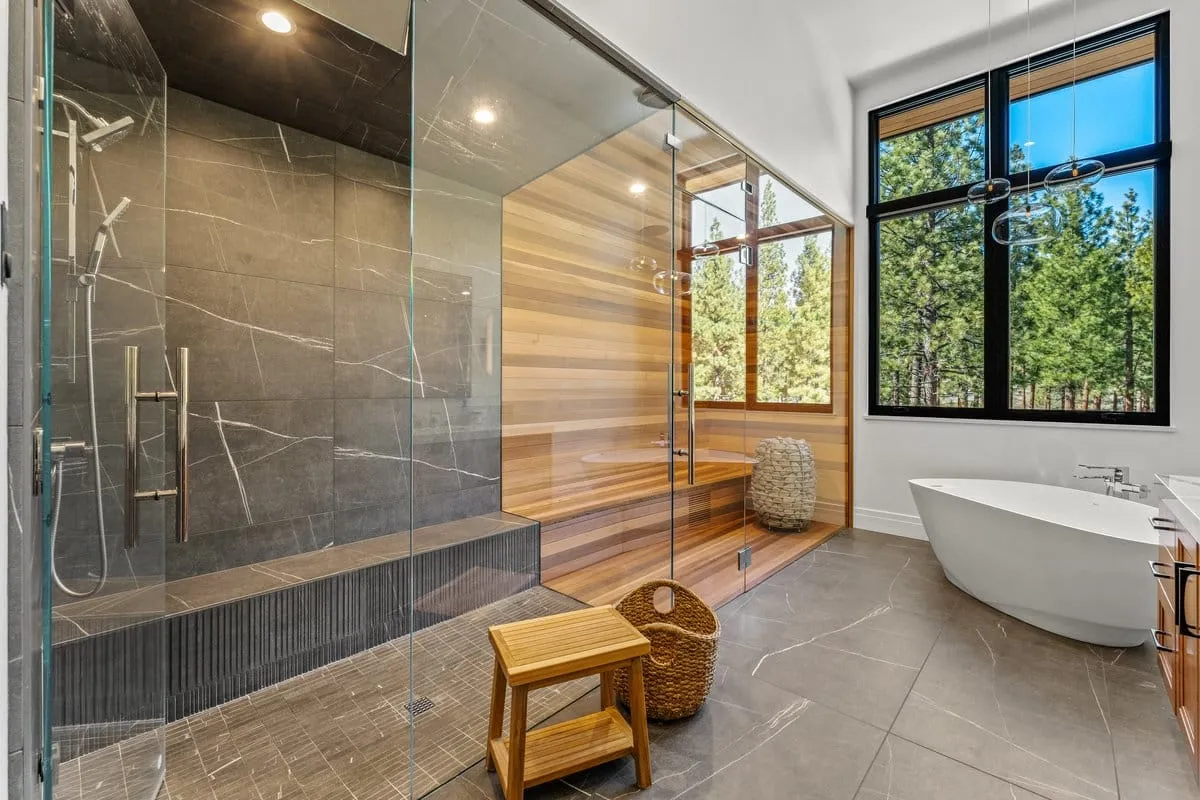 Bathroom with a glass-walled shower of dark veined tile, a cedar-lined room with a bench behind it and a freestanding tub under a window