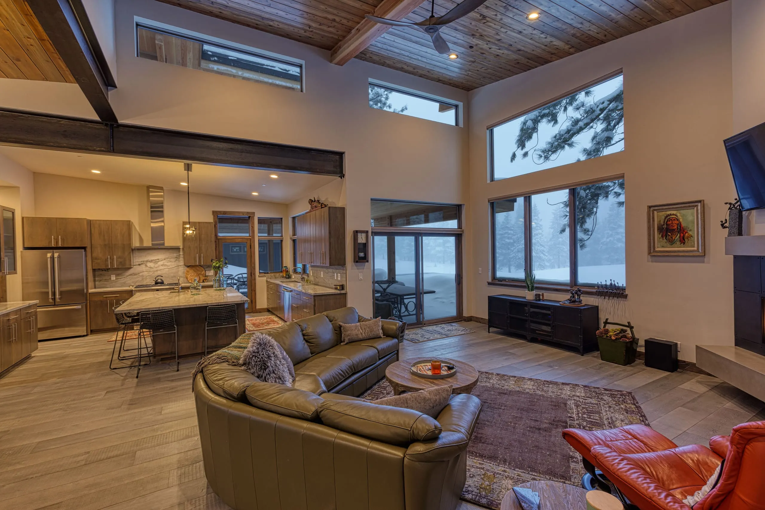 Interior great room with vaulted wood ceiling, steel beam, tall windows, open kitchen and leather sectional sofa
