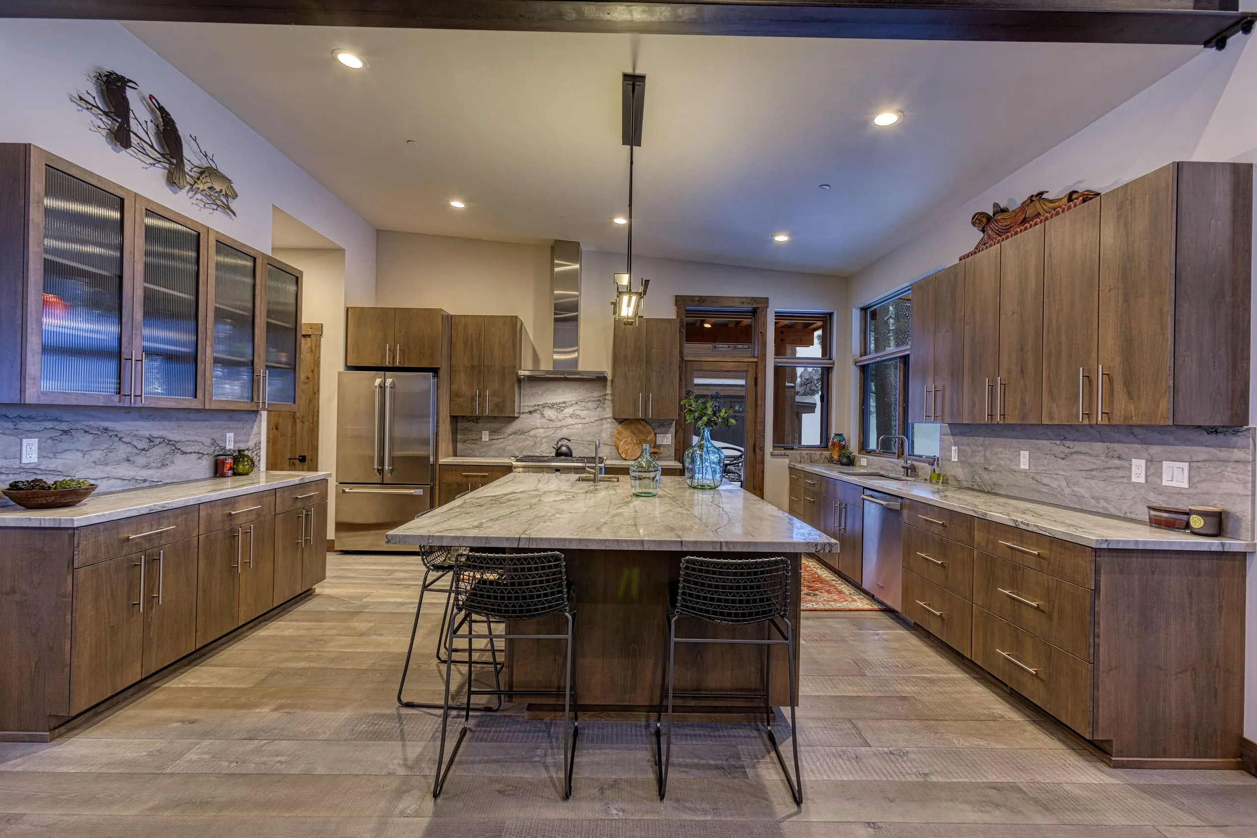 Kitchen with dark wood cabinets, stone-slab backsplash, large island with bar stools and plank flooring