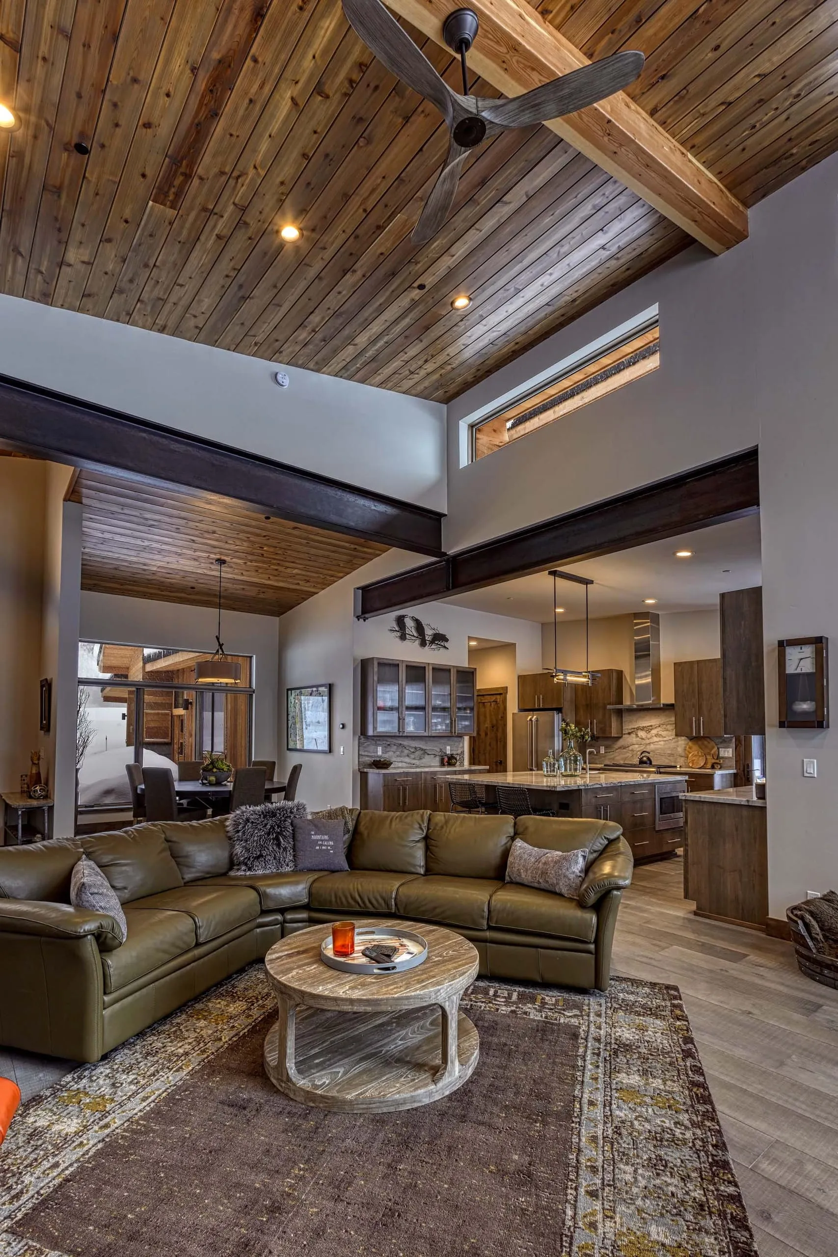 Tall living room with wood ceiling, exposed beams, clerestory windows, sectional sofa and kitchen beyond