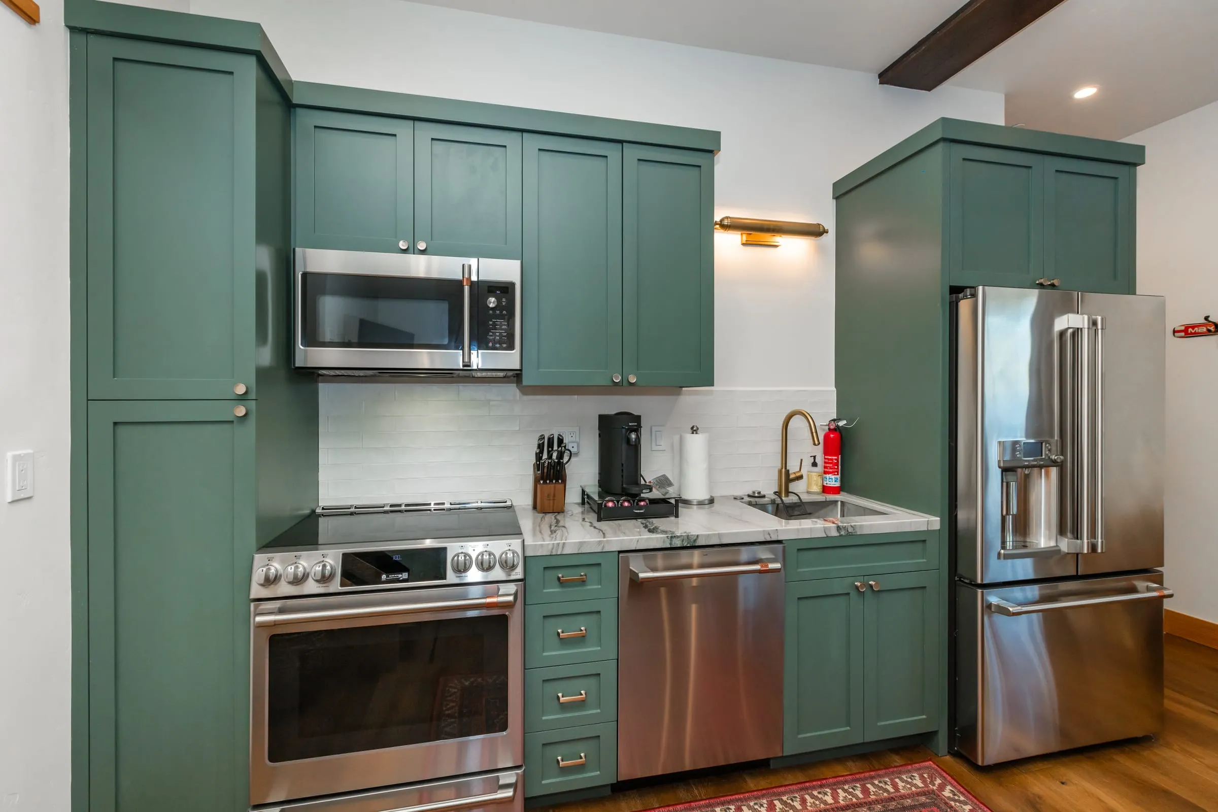 Kitchen with green cabinets, a stainless range and refrigerator, a marble-look counter and a white tile backsplash
