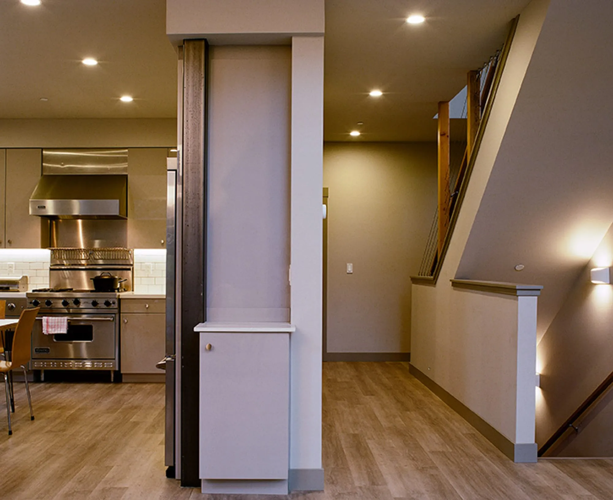 Interior with open kitchen and range at left, a structural column, and a staircase with wall sconces