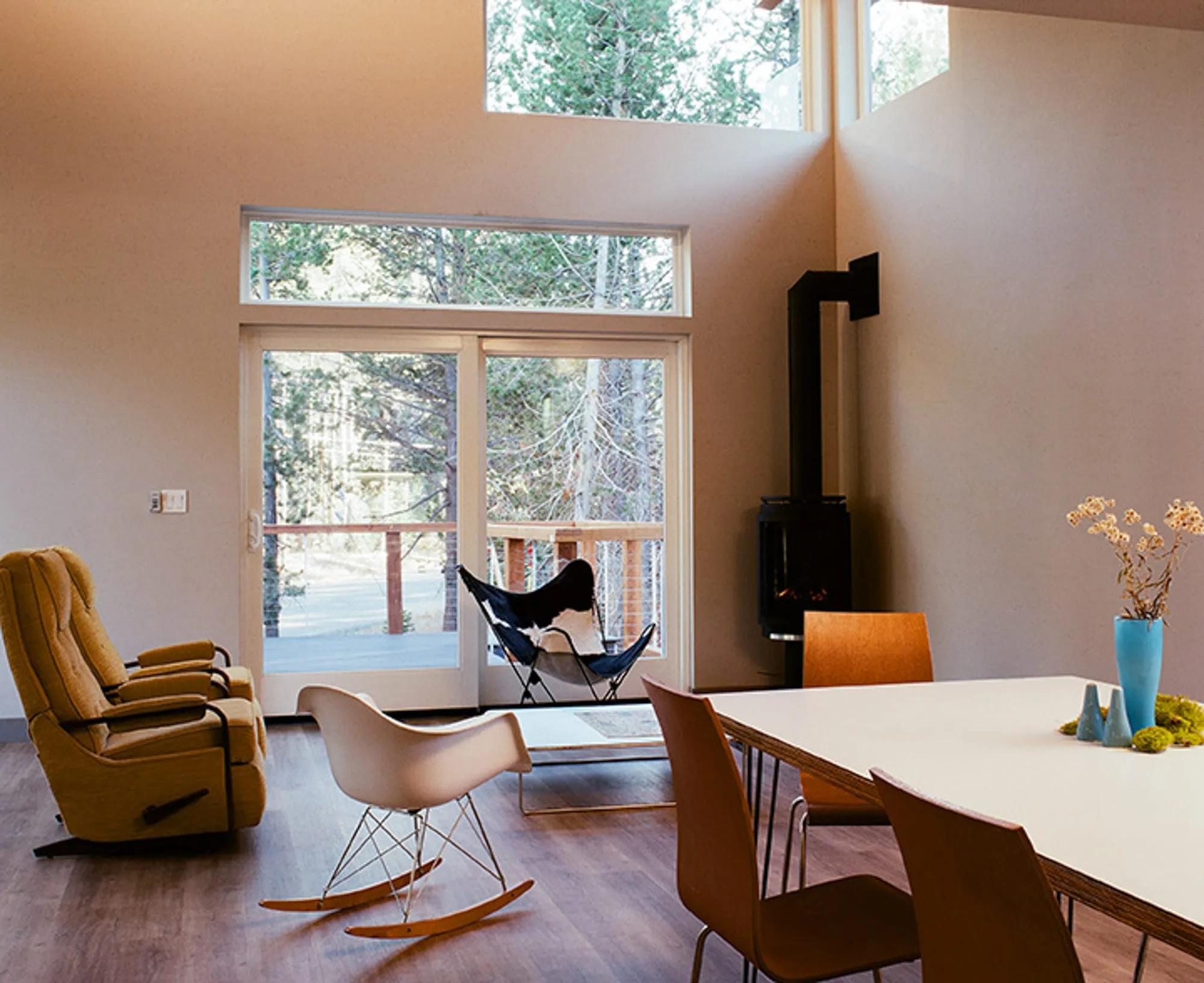 Living and dining area with sliding glass doors to a deck, clerestory windows, black stove and wood chairs