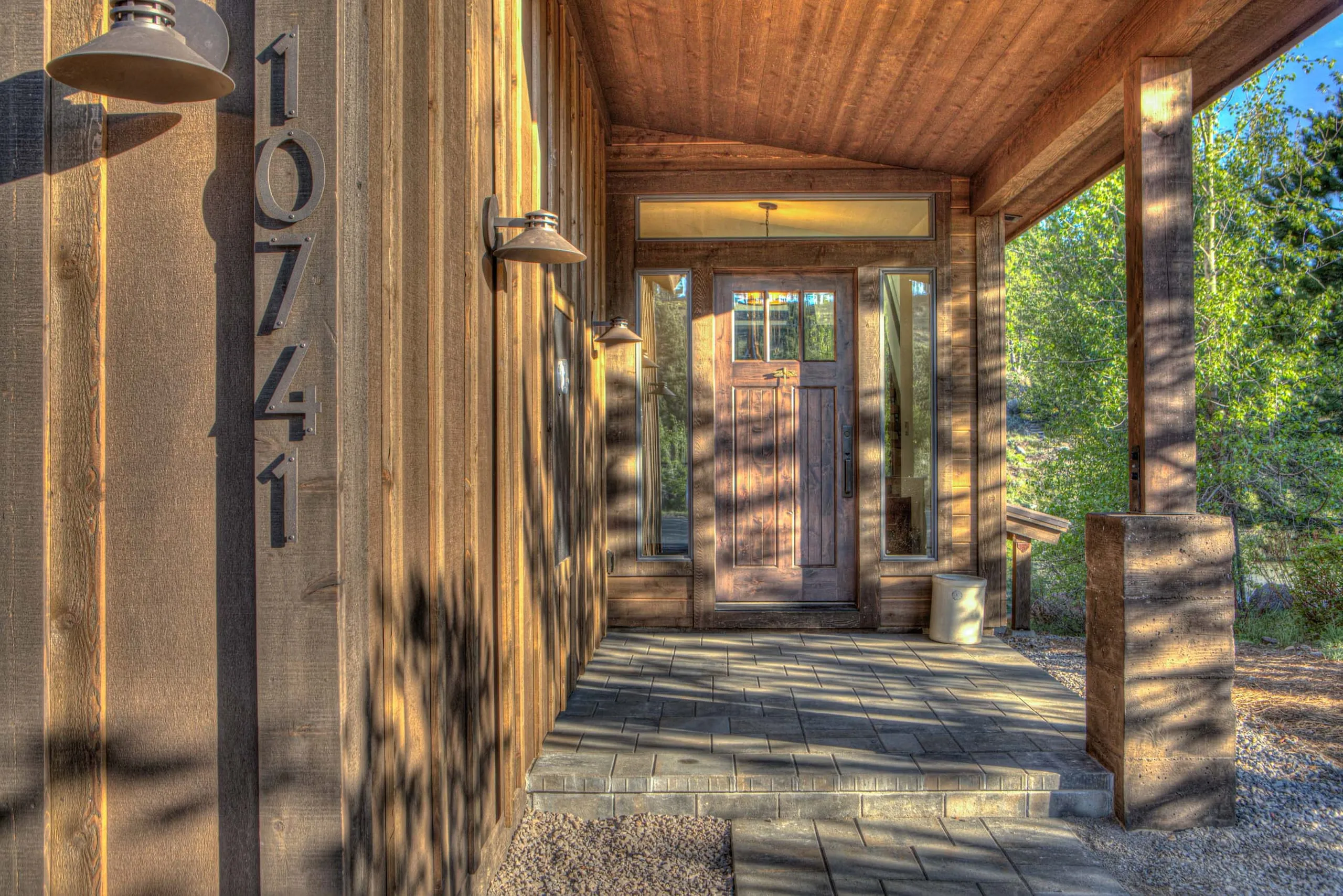 Covered entry porch with a wood front door, board-and-batten siding and a paver walkway