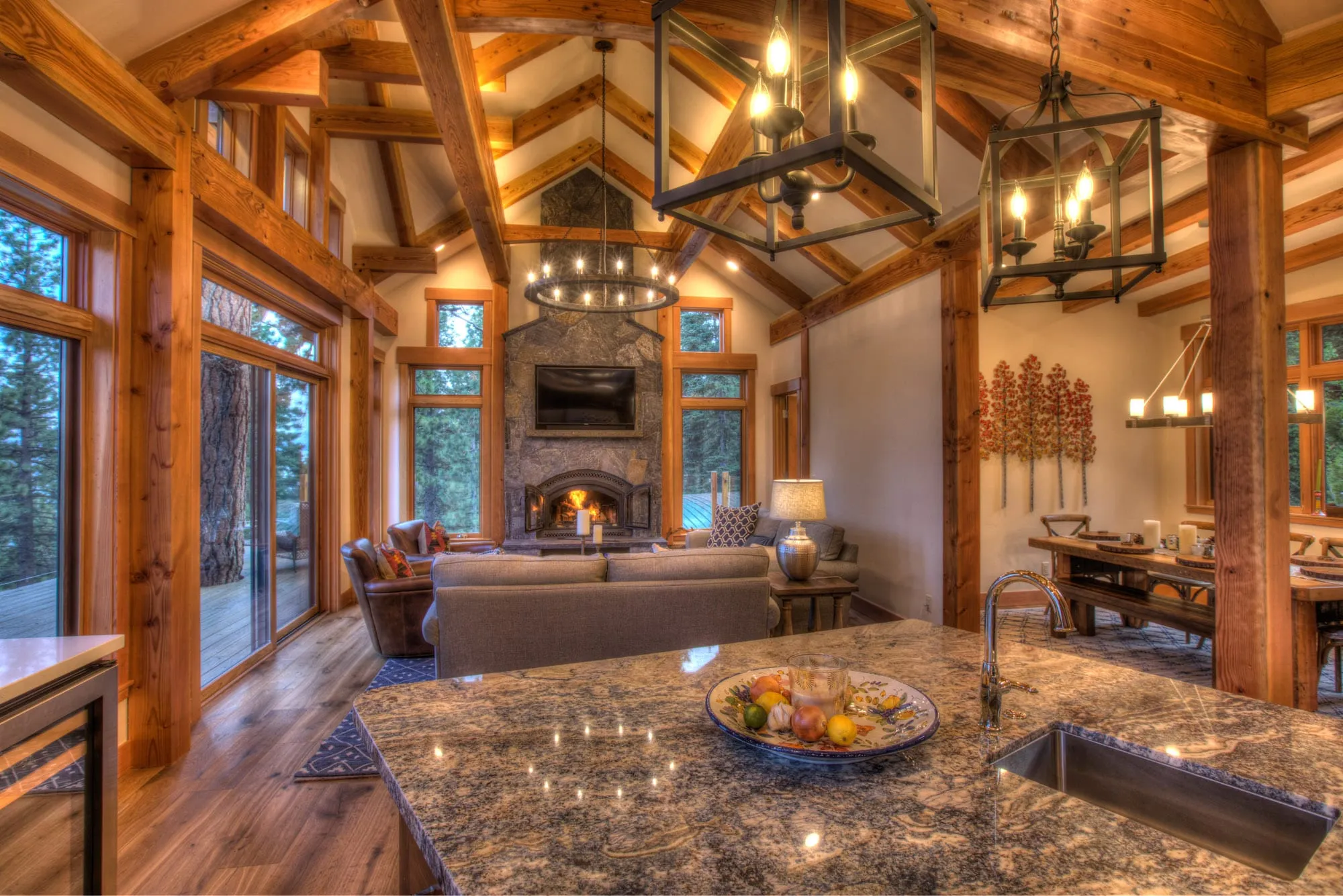 Great room with timber posts and trusses, stone fireplace, lantern lights and granite kitchen island in foreground