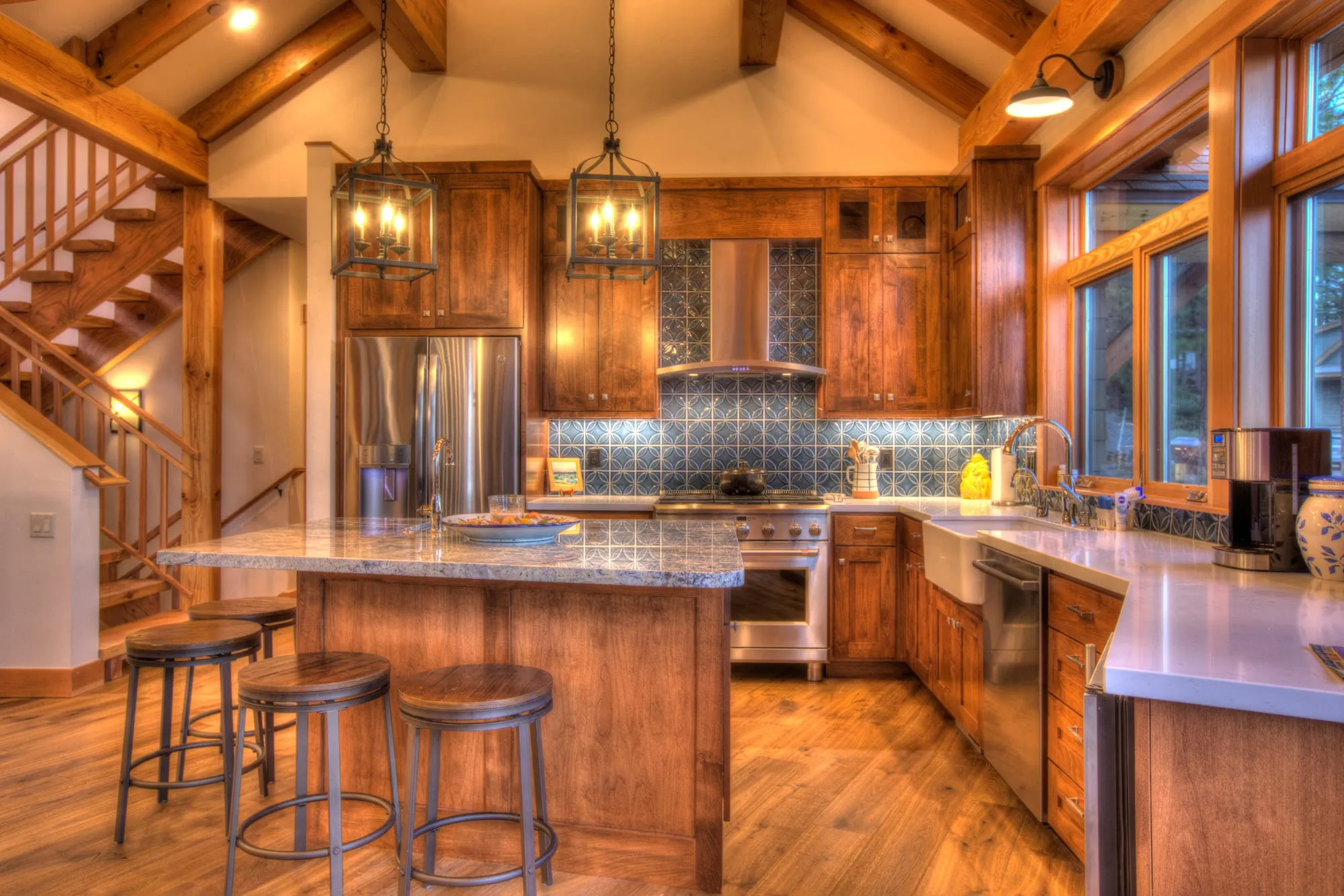 Kitchen with timber beams, lantern pendants, a stone-topped island with stools, patterned tile backsplash and a staircase
