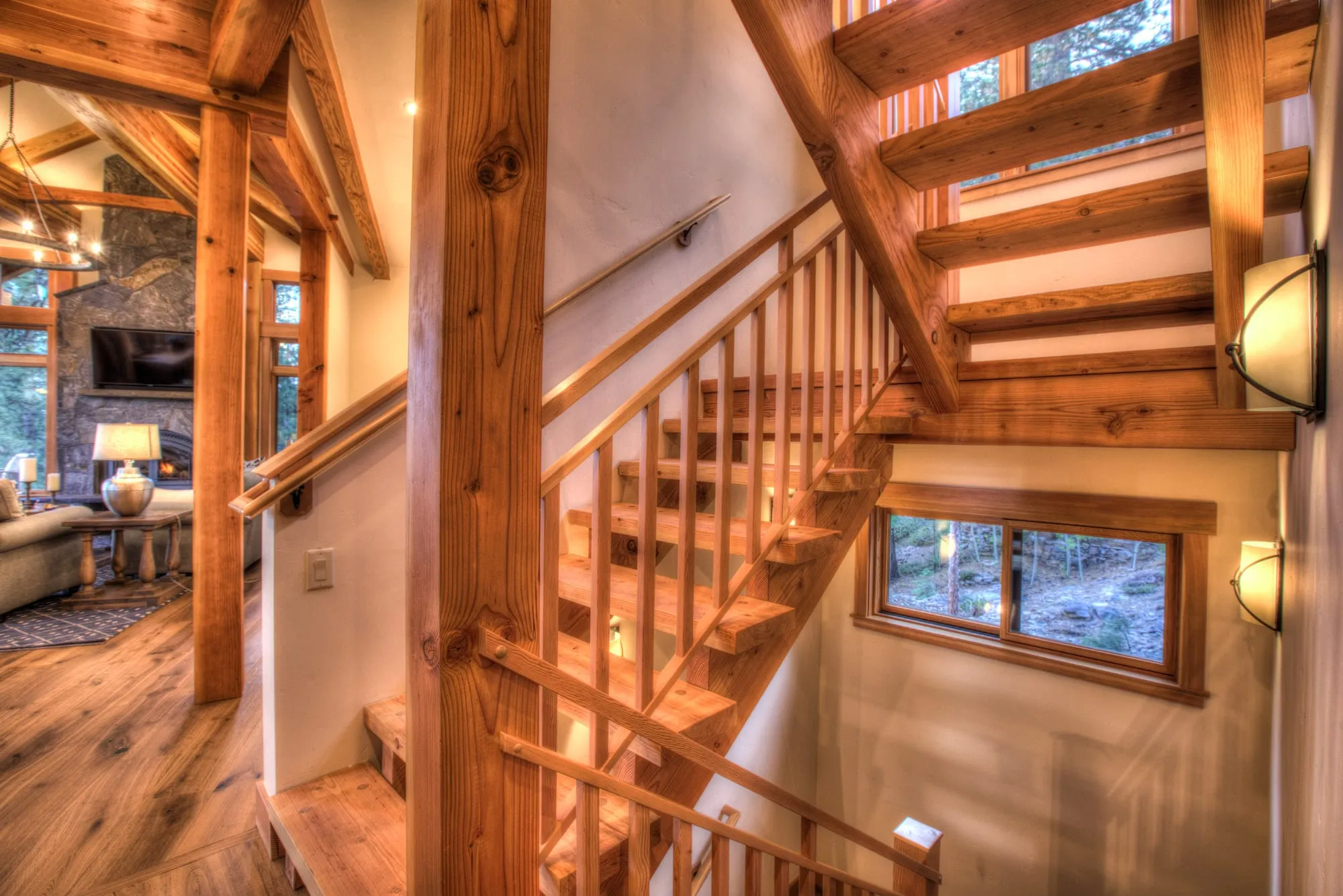 Timber-frame staircase with wood posts and railings leading down, with the great room visible beyond