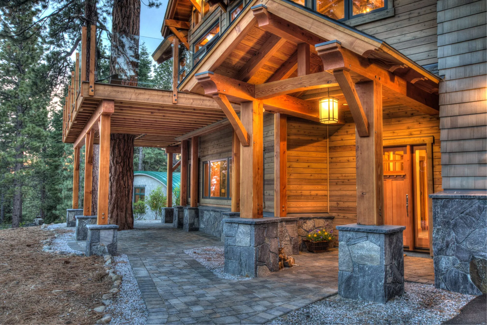 Covered timber entry porch with heavy beams and stone piers, paver walkway and a wood front door