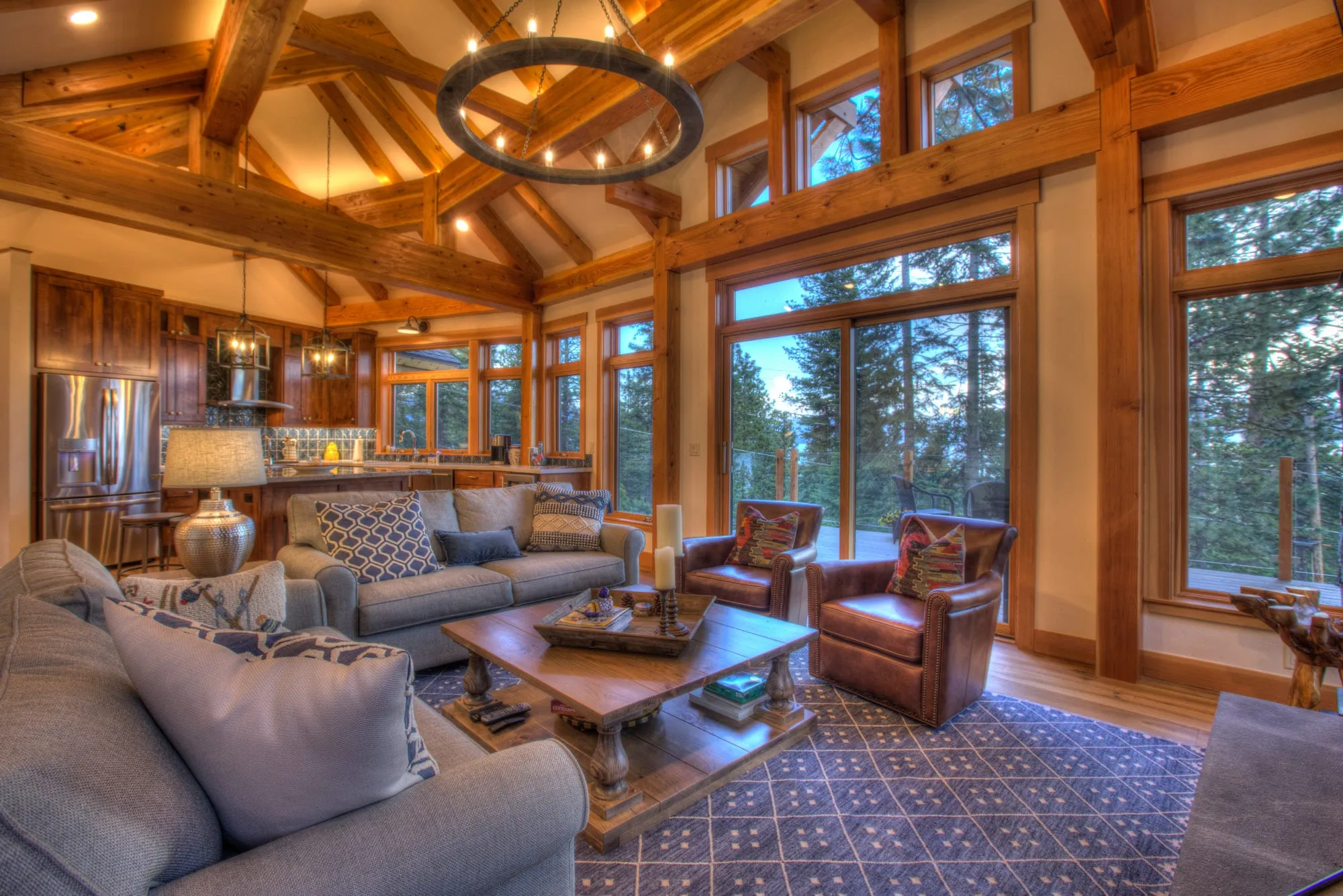 Vaulted great room with exposed timber trusses, leather chairs, sofas and large windows onto the forest