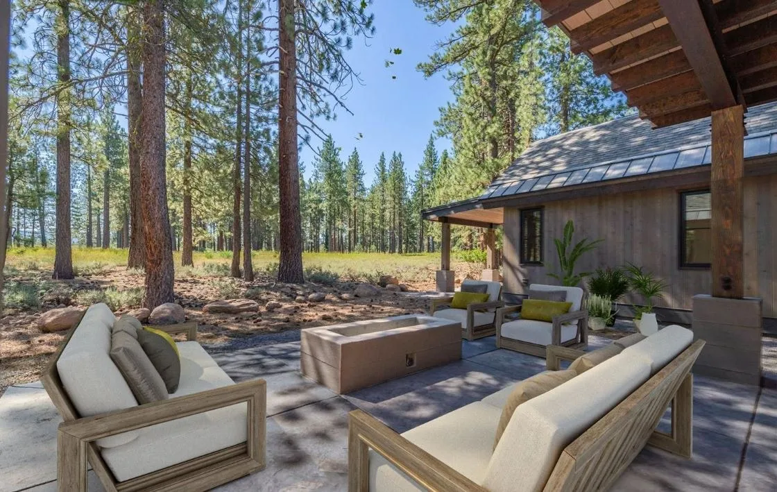 Terrace with a fire table and outdoor sofas under a timber-framed roof, looking out to a meadow and pine forest