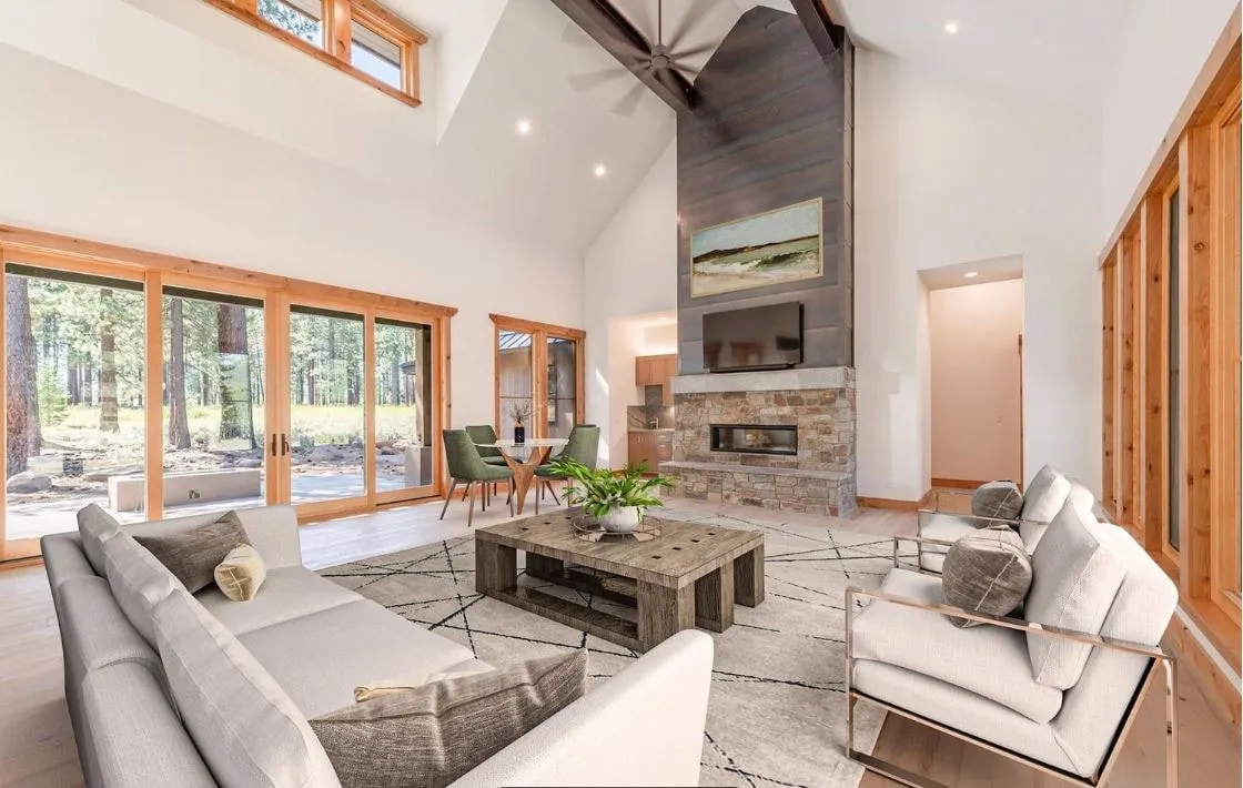 Vaulted living room with a stone and wood fireplace wall, clerestory windows, wood-framed glass doors and a dining table