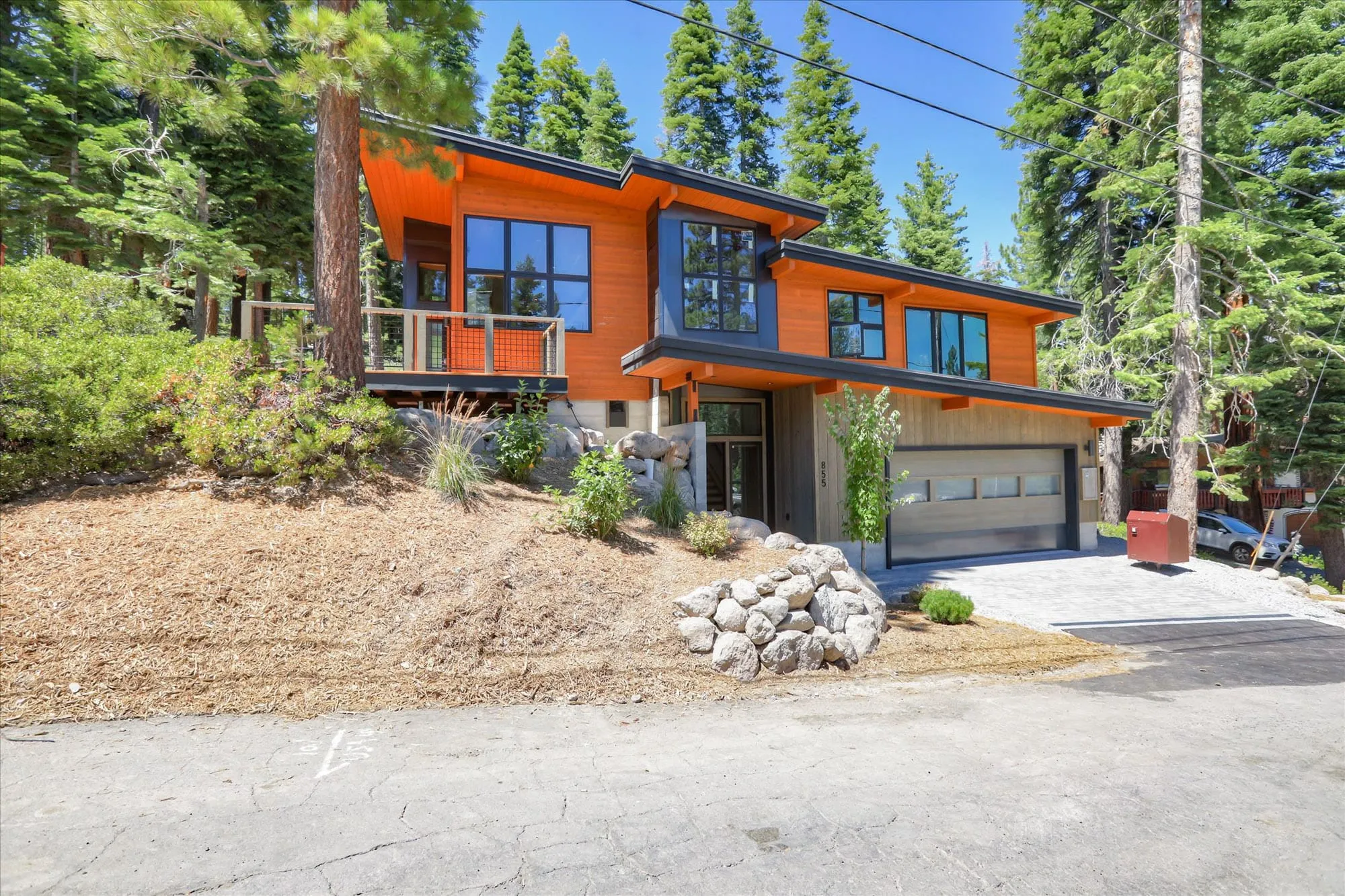 Front view of a modern hillside home with orange cedar siding, dark metal roof, boulder retaining wall and attached garage