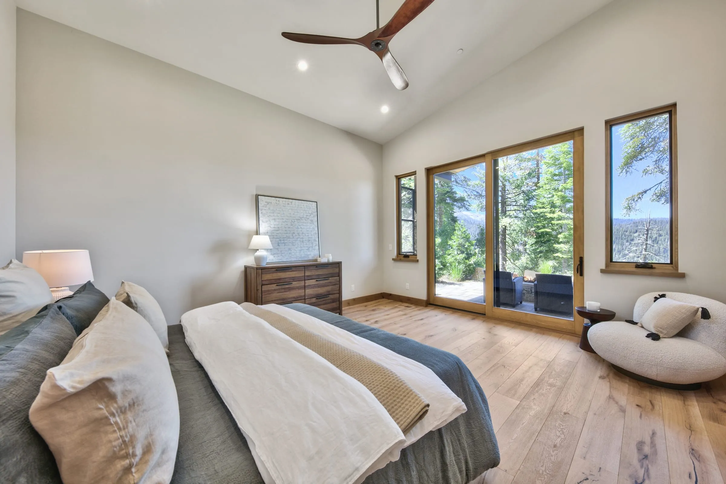 Vaulted bedroom with wide-plank floors and glass doors and windows to a deck and the forest