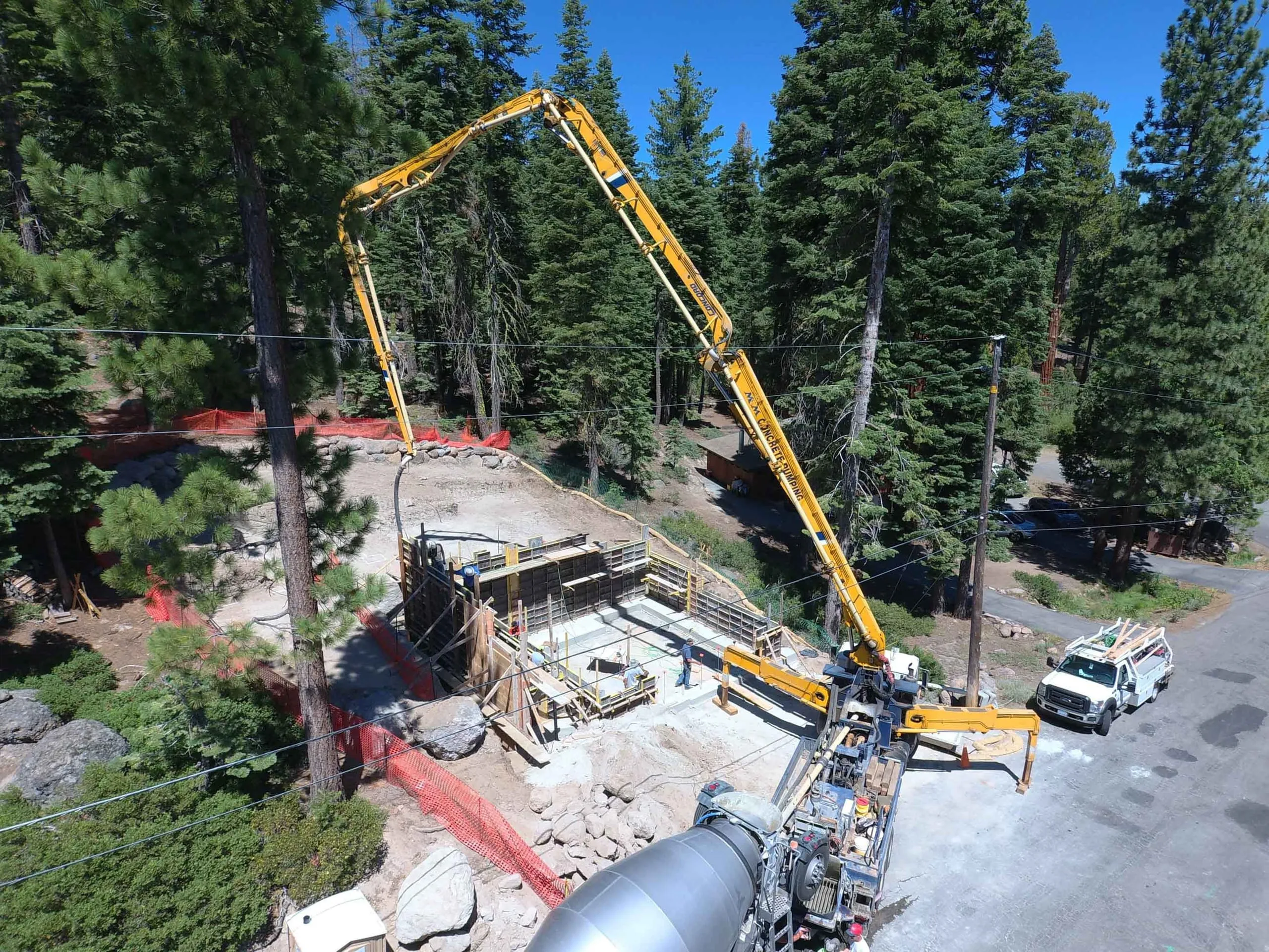 Construction photo: concrete pump boom and mixer truck pouring a retaining wall at a forested hillside job site