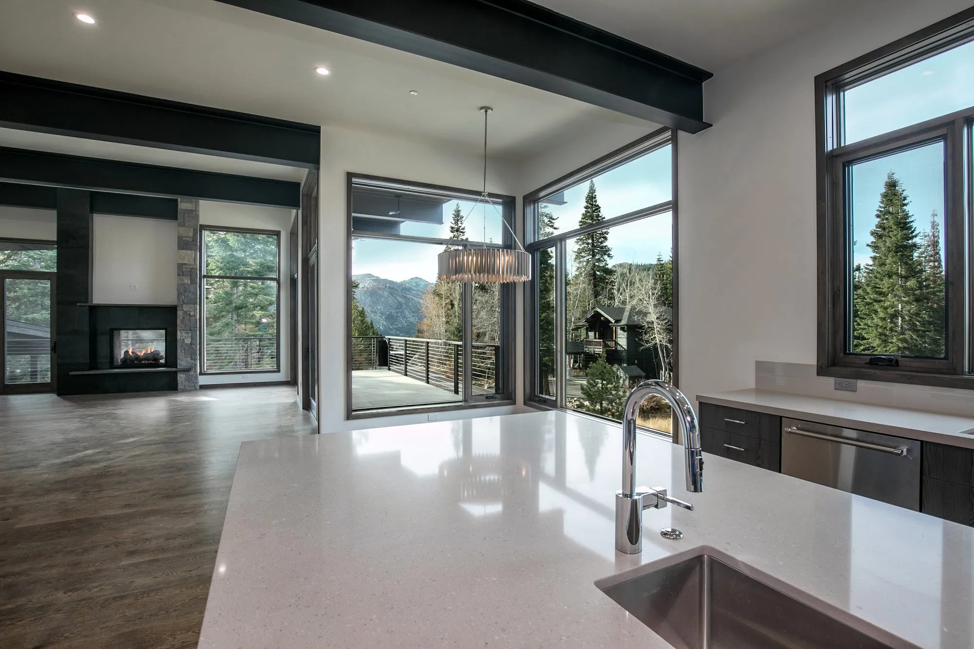 Interior view from a stone-topped kitchen counter to a see-through fireplace and glass doors opening to a deck and mountains