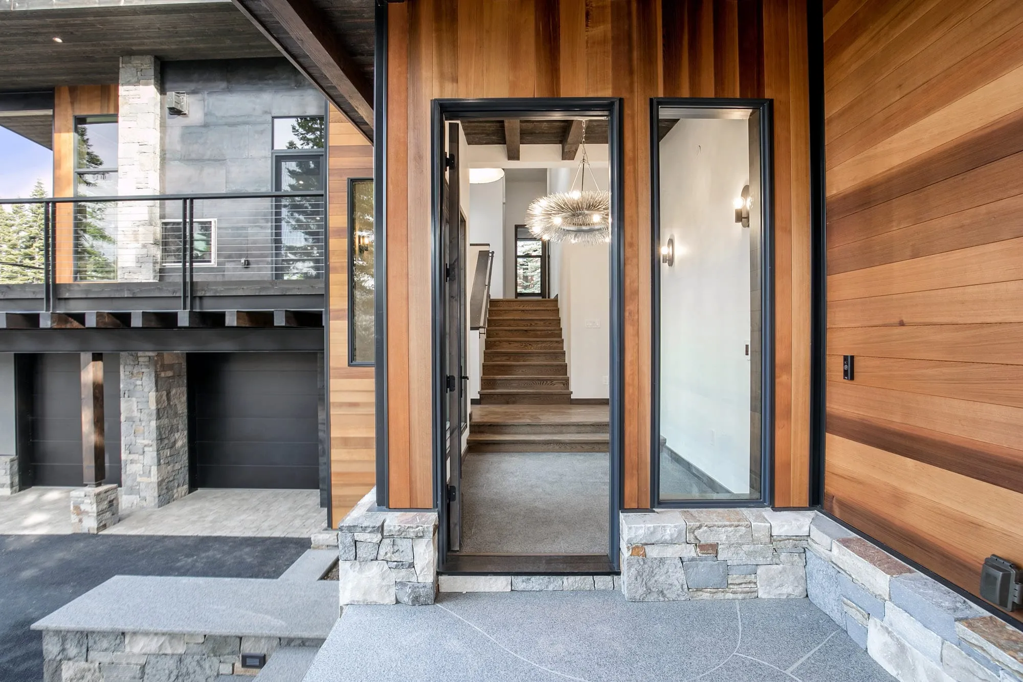 Entry detail with a black-framed glass door and sidelight in cedar siding, stone steps, and a staircase visible inside