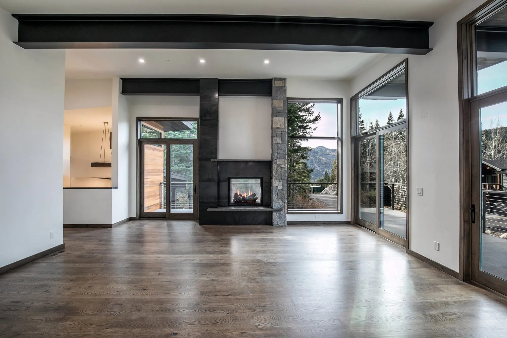 Living room with dark steel beam, see-through fireplace, tall glass doors to a deck and mountain views, dark wood floors