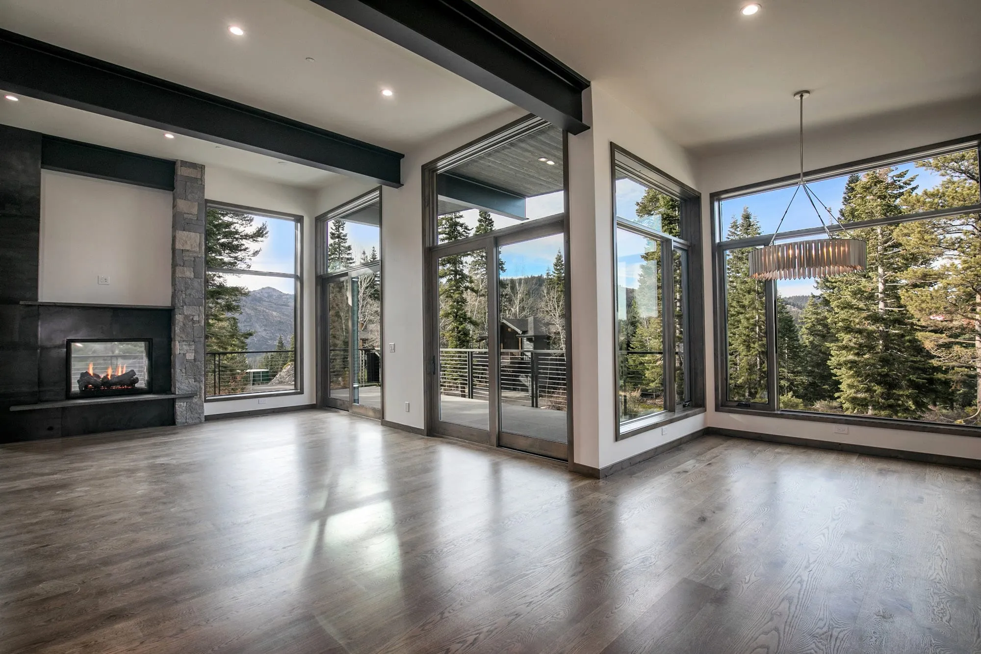 Open living and dining space with large corner windows, glass doors to a cable-rail deck, fireplace and wide-plank floors