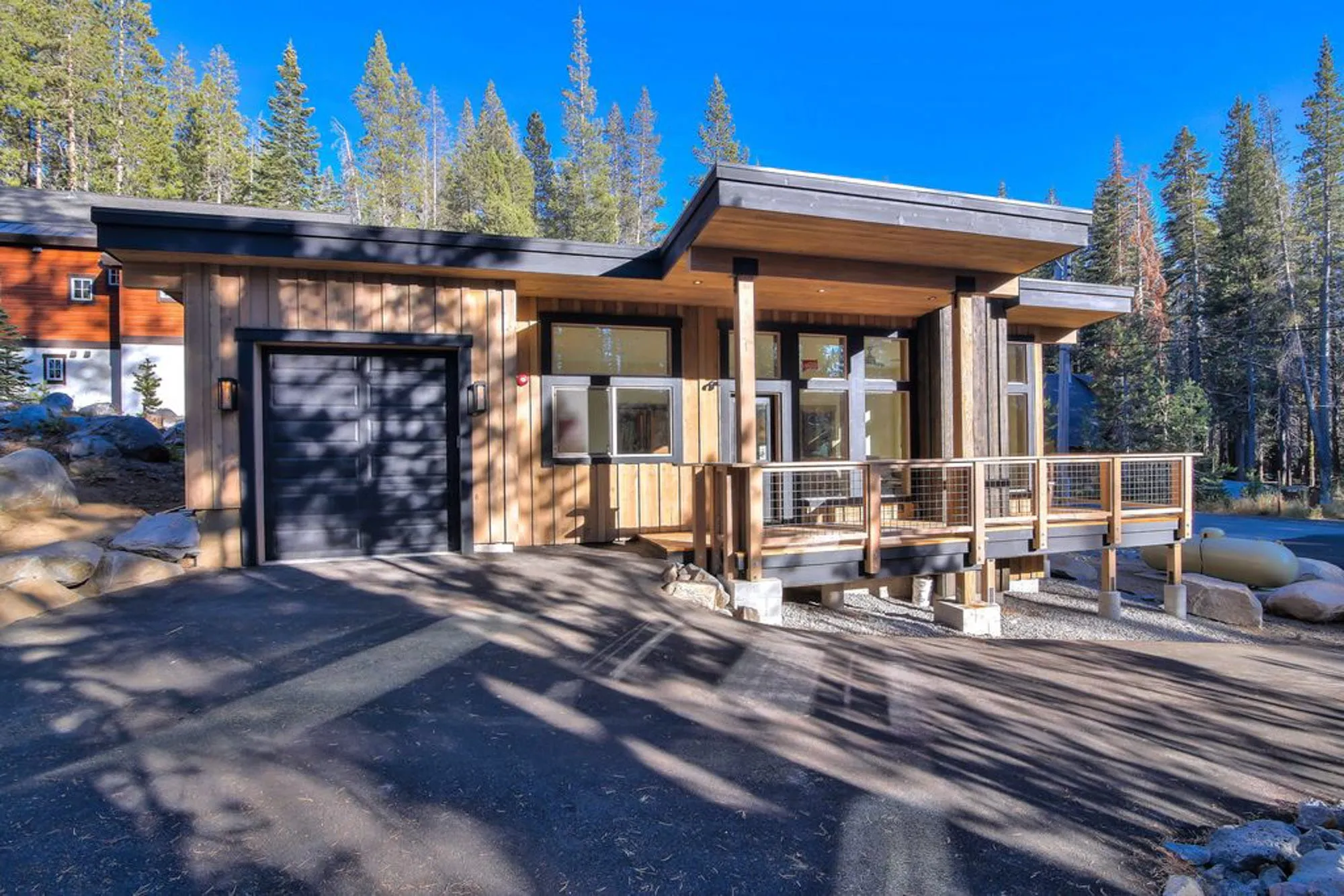 Tiny home front with black garage door, vertical wood siding, flat overhanging roof and a cable-rail deck