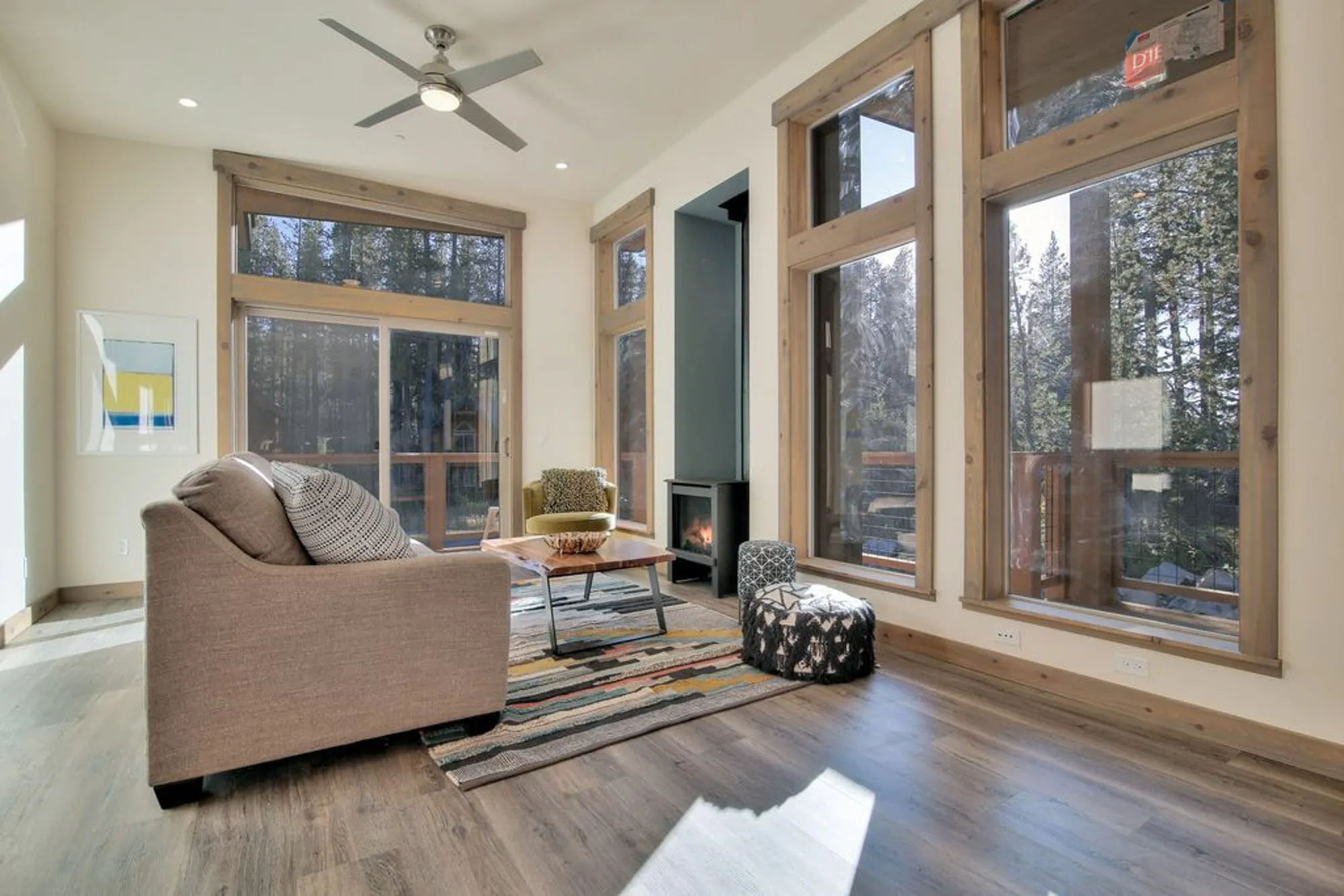 Small living room with tall windows, a gas stove, patterned rug and a sliding door to the deck among trees