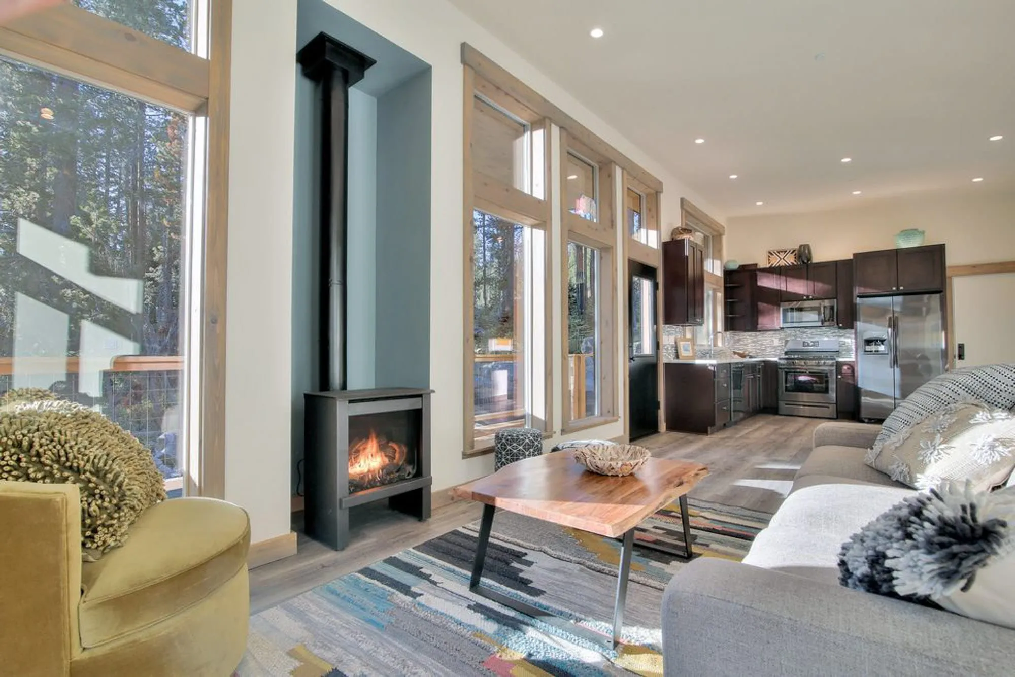 Open tiny home interior with gas stove in a teal alcove, live-edge coffee table and kitchen beyond